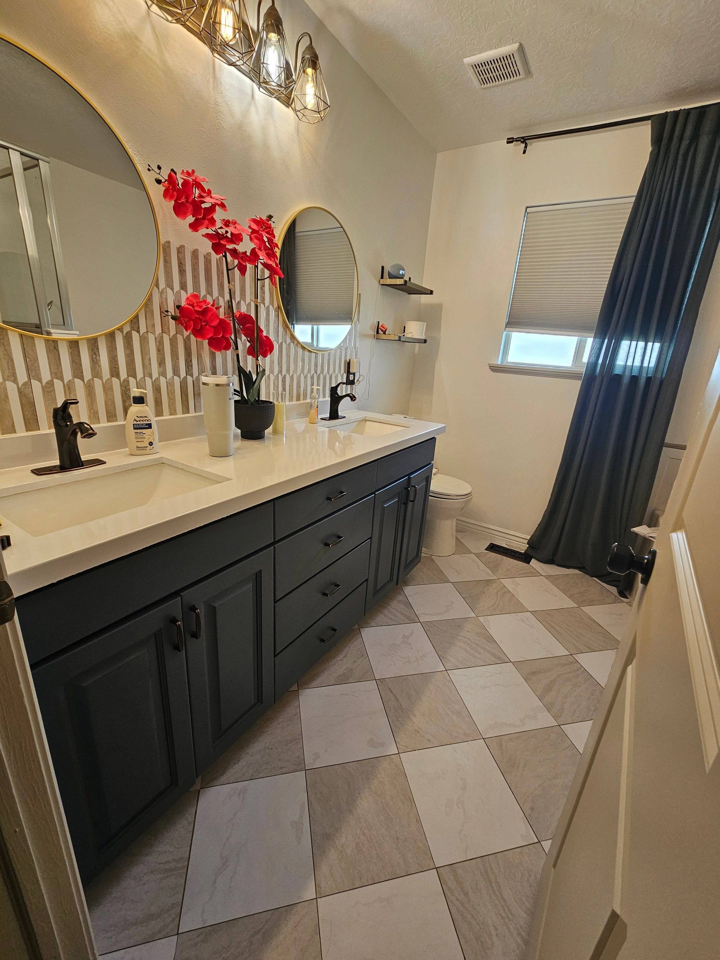 Completed primary bathroom makeover with navy vanity, white epoxy countertops, round mirrors, and oil-rubbed bronze fixtures