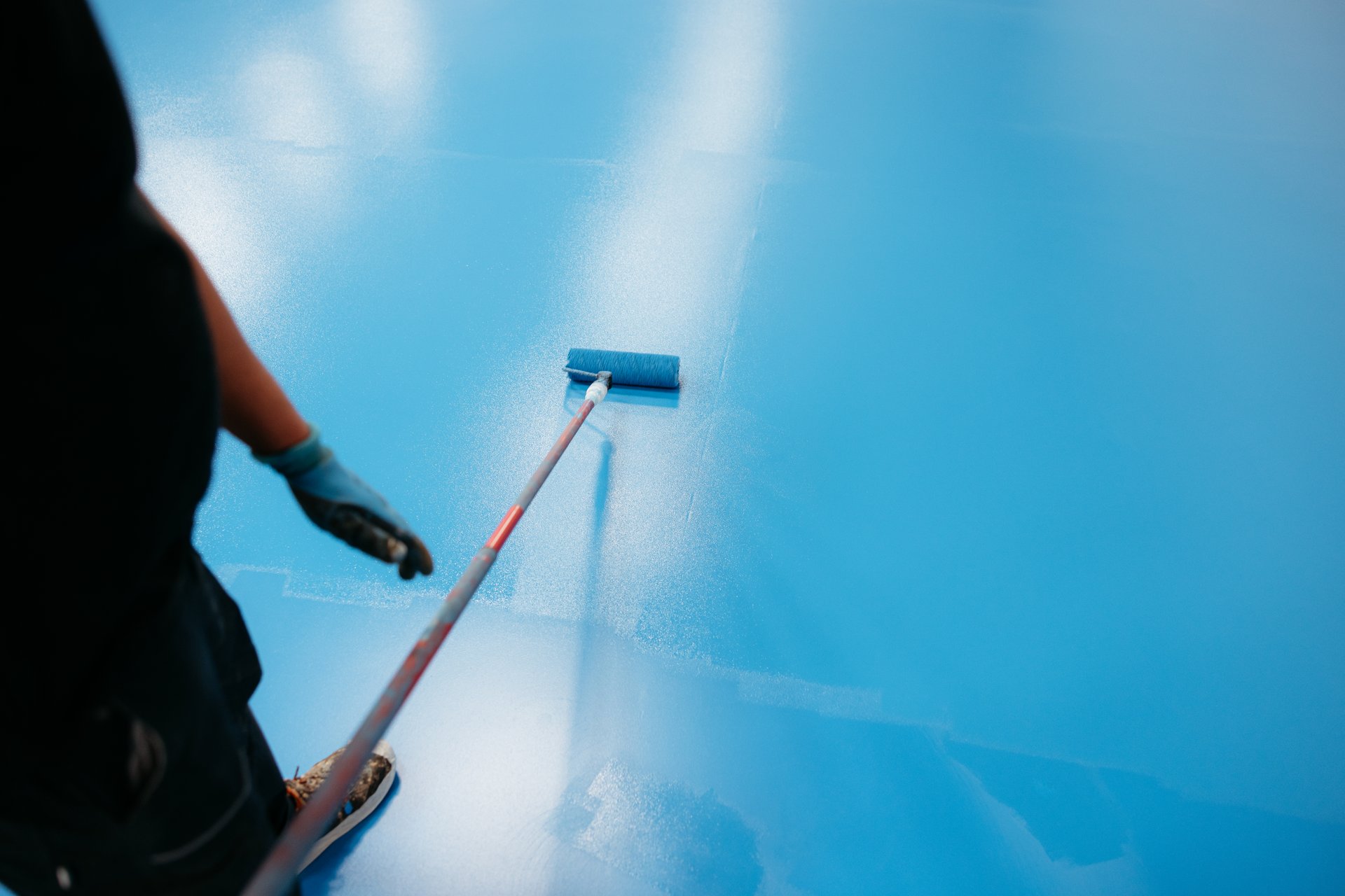 Construction worker applying blue epoxy resin on rubber flooring using a roller