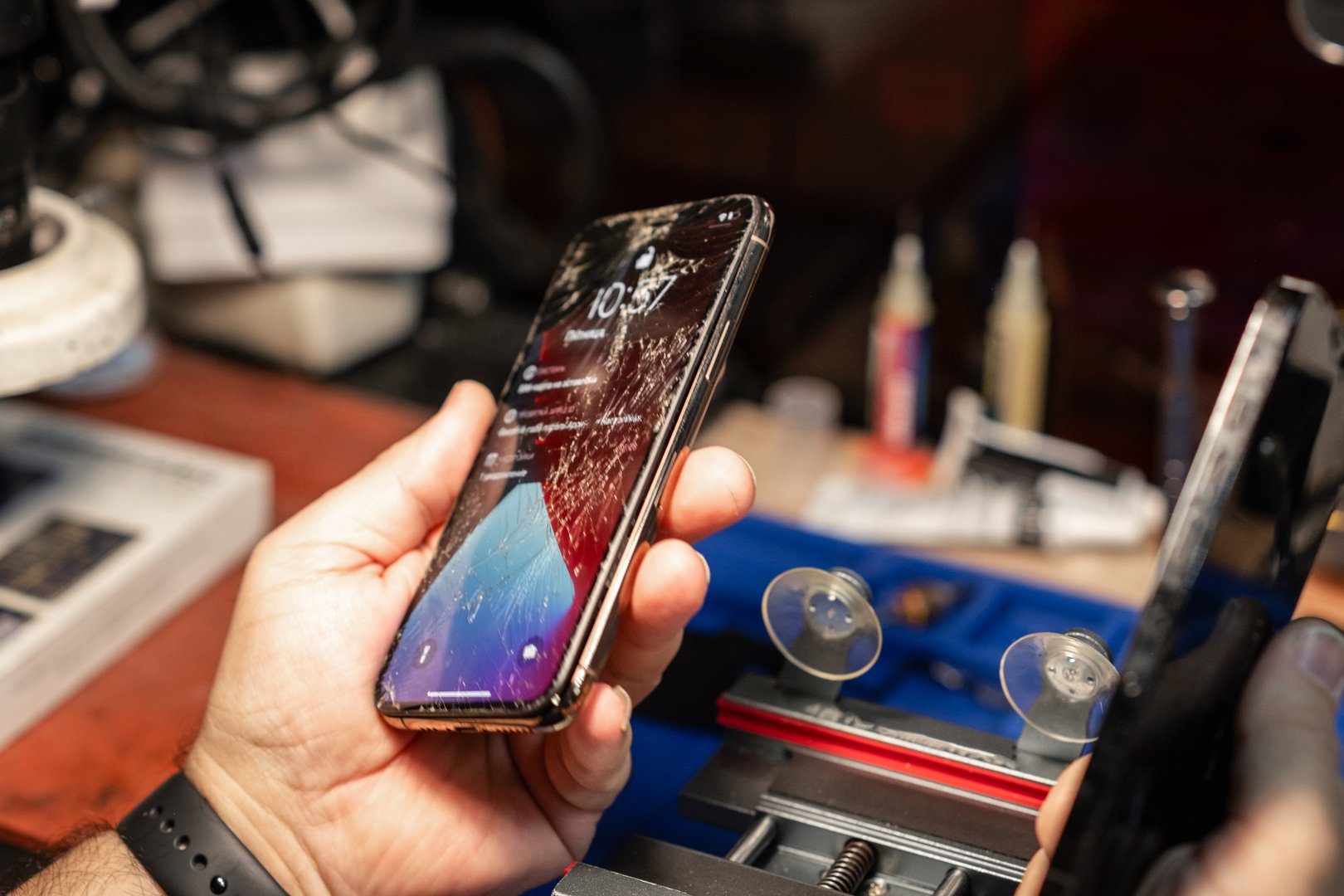 A technician is inspecting a smartphone with a cracked screen at a bustling phone repair service during the day.