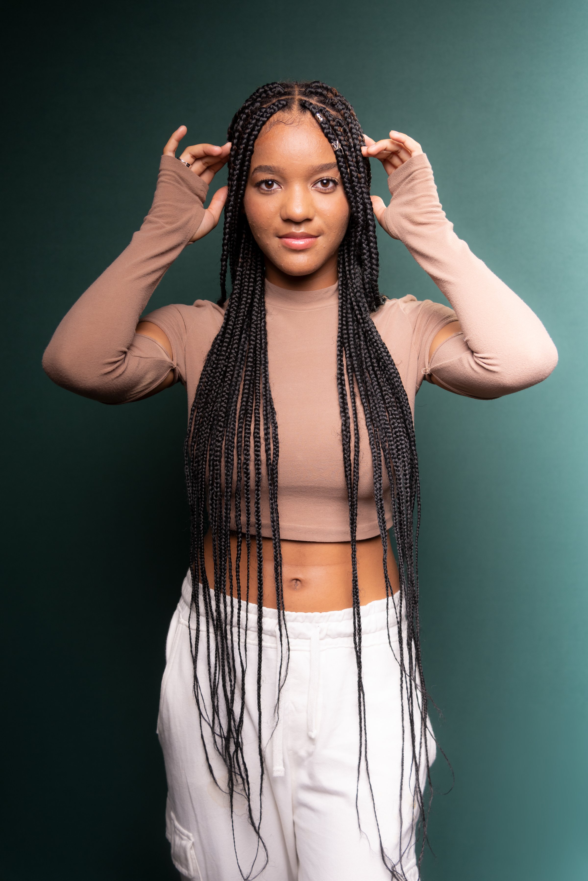 Portrait of beautiful young woman, standing, with big braids in her hair. Isolated on dark green background