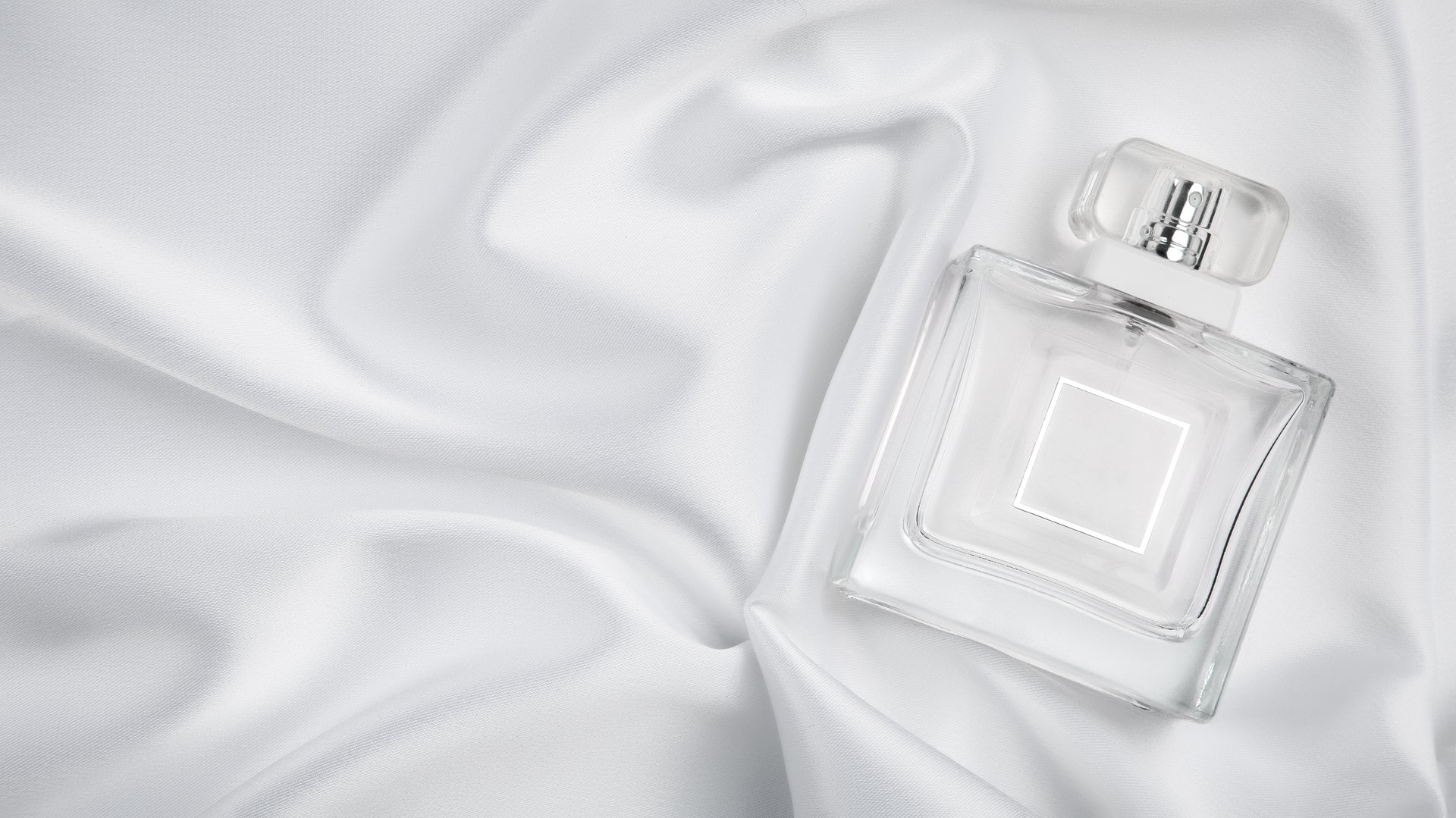 Perfume bottle on white satin folded fabric background. Scent fragrance cosmetic beauty product.