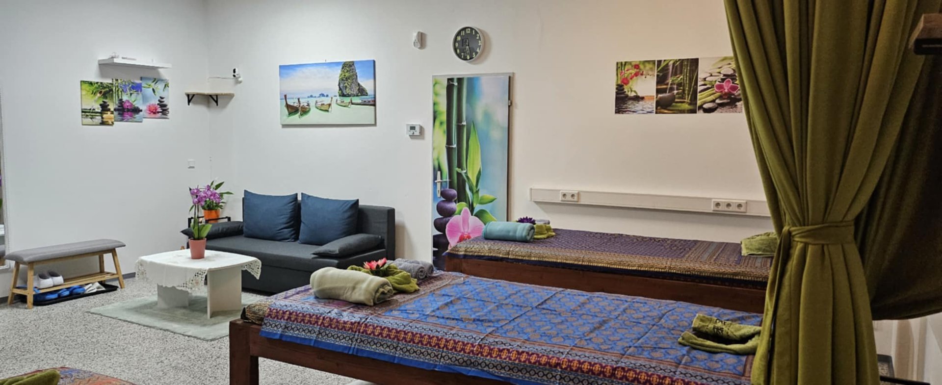 Tranquil massage room with two covered tables, a small couch, and soothing wall art. Towels are neatly placed on each table.