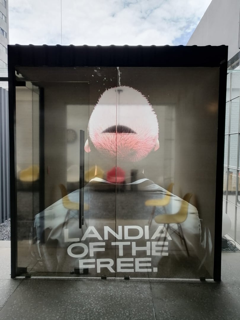 Large poster of a man with a high fade hairstyle on a glass exterior, text reads "LANDIA OF THE FREE."