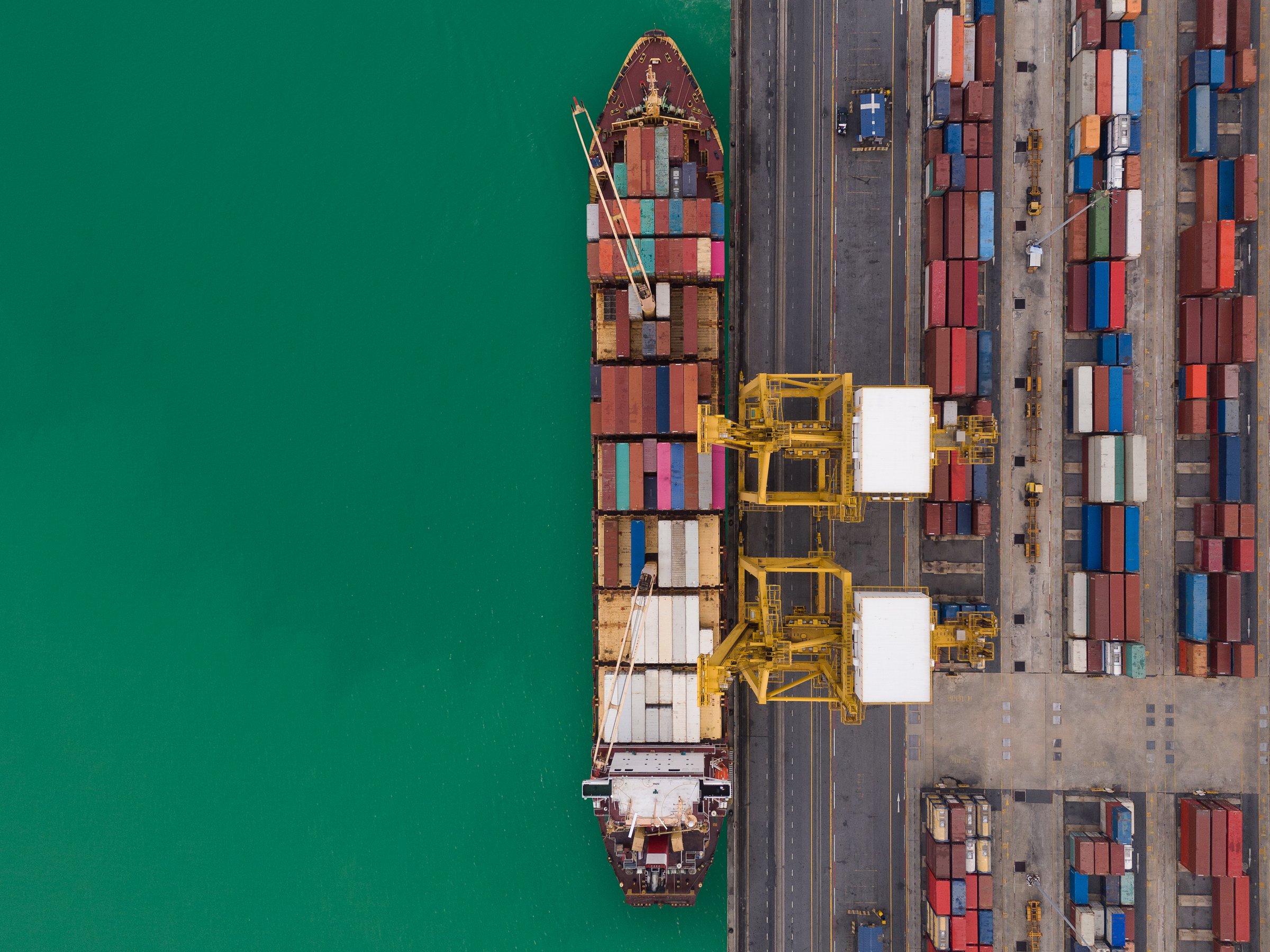 Aerial top view over international containers cargo ship at industrial import-export port prepare to load containers with big container loader ship vessel. global transportation and logistic business.