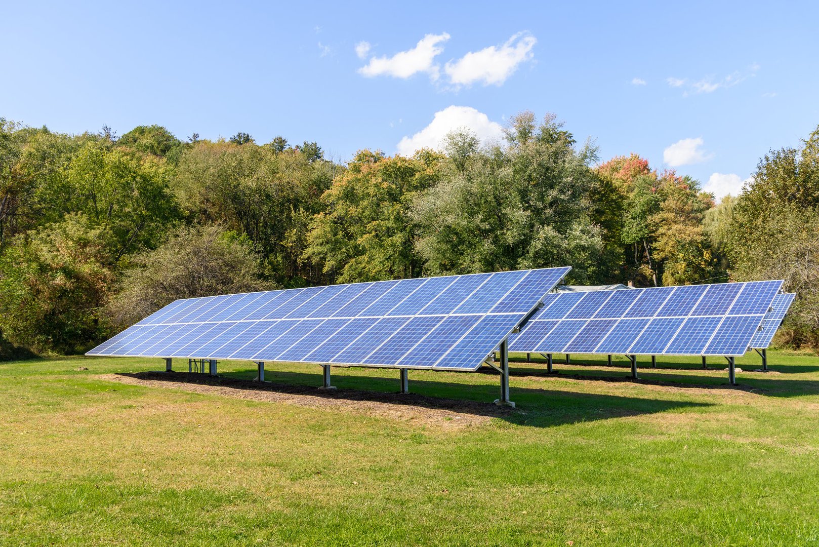 Rows of solar panels with trees in background in the countryside on a clear autumn day. Upstate New York, United States.