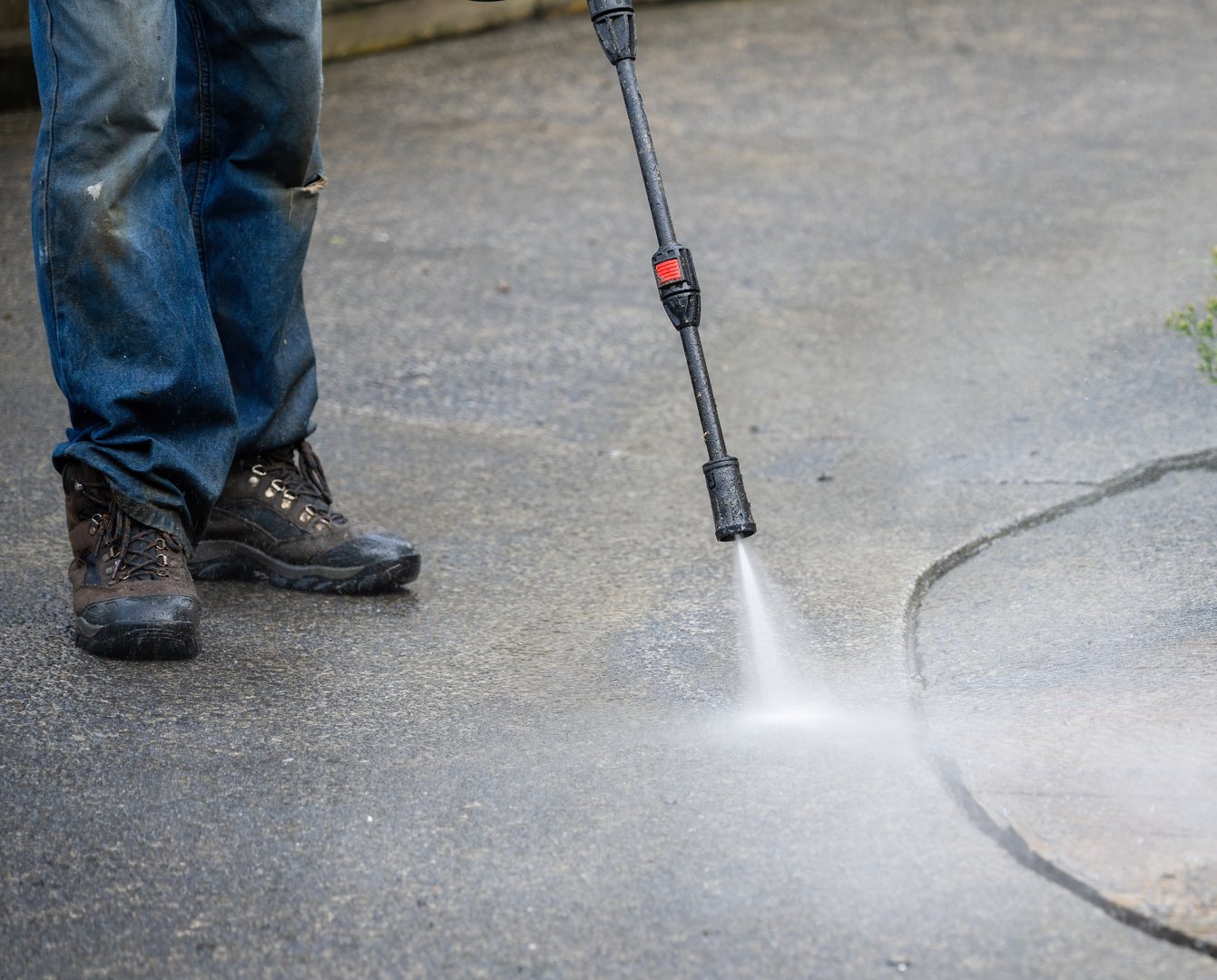 Worker cleaning pavement using an electric water blaster.