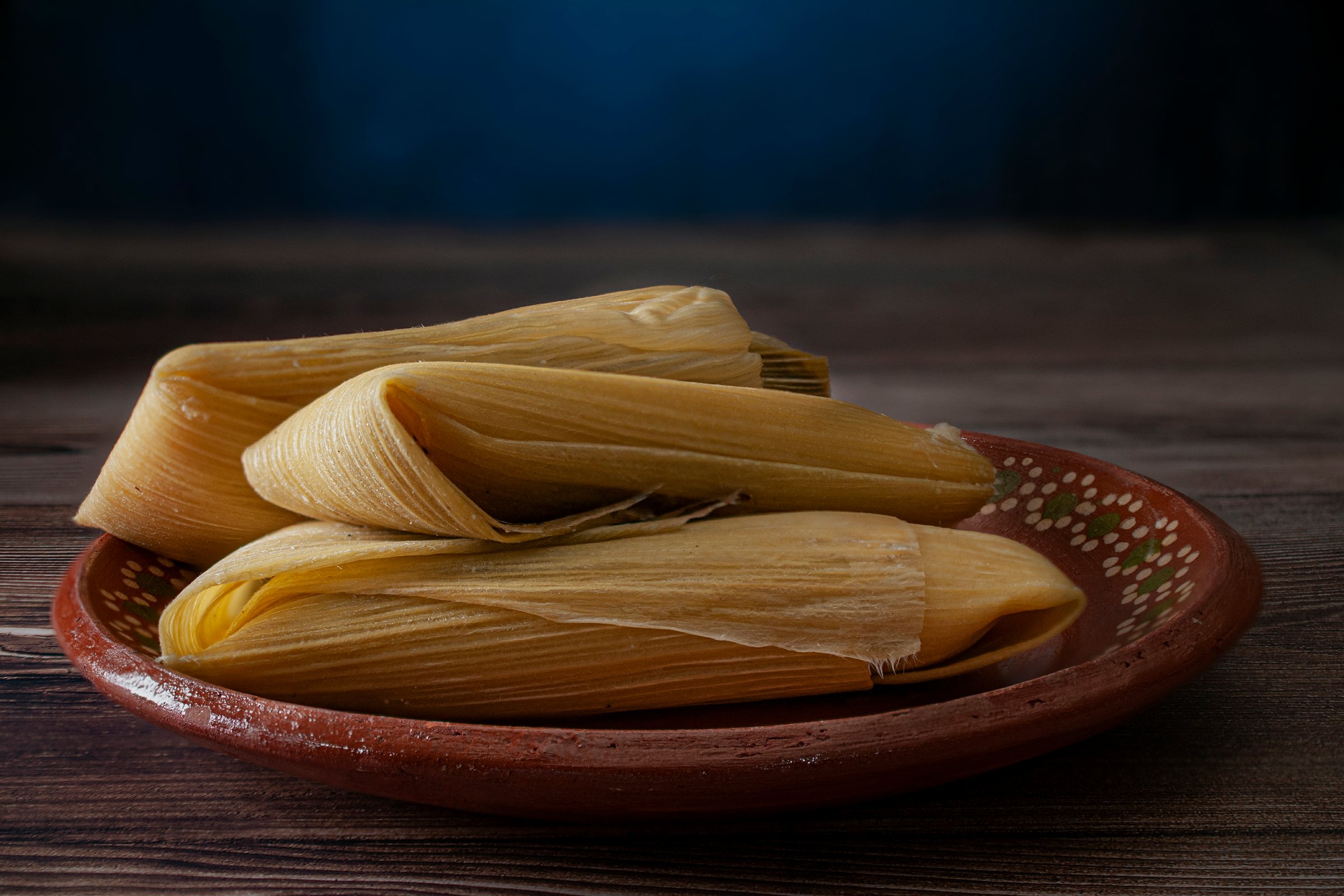 corn tamales with cheese in a mexican clay plateand on a wooden table, side view shot