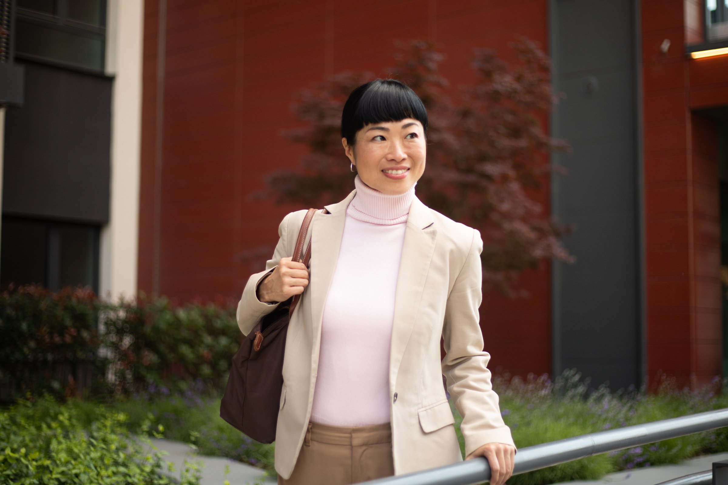 Asian businesswoman walking outside office building, holding bag and smiling