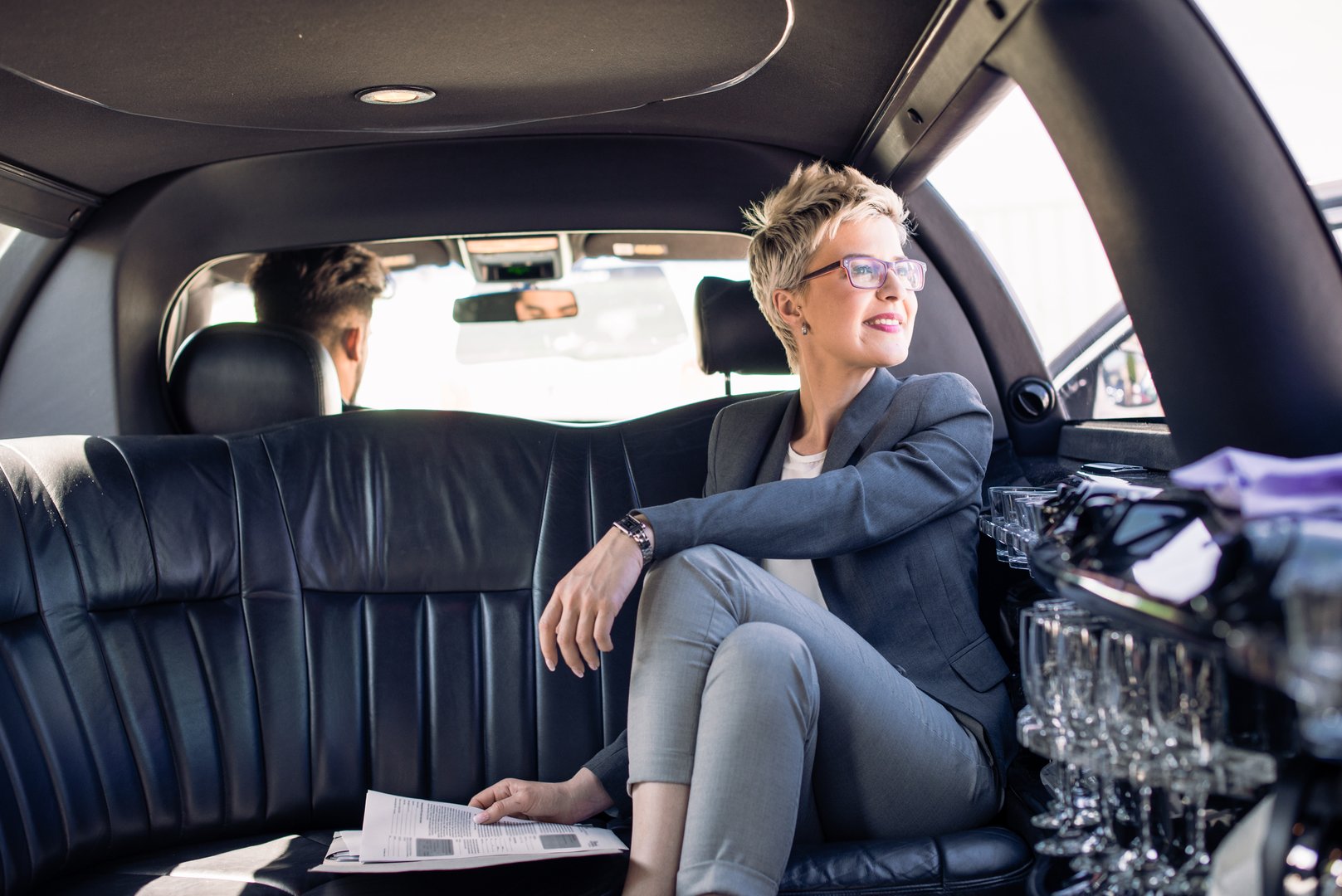 Young business woman is sitting in limo with her driver, looking trough the window