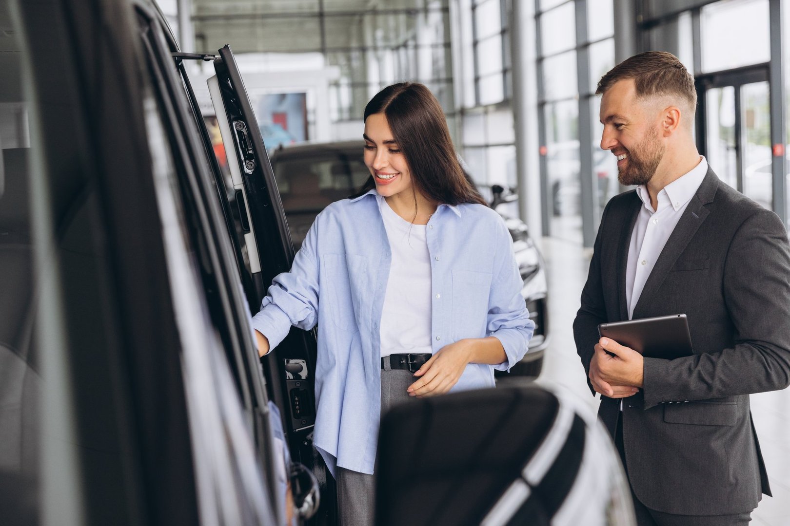 Car Sales Manager Showing Auto Minivan To Caucasian Lady Buyer Standing In Luxury Automobile Dealership Store. Buying Vehicle Concept