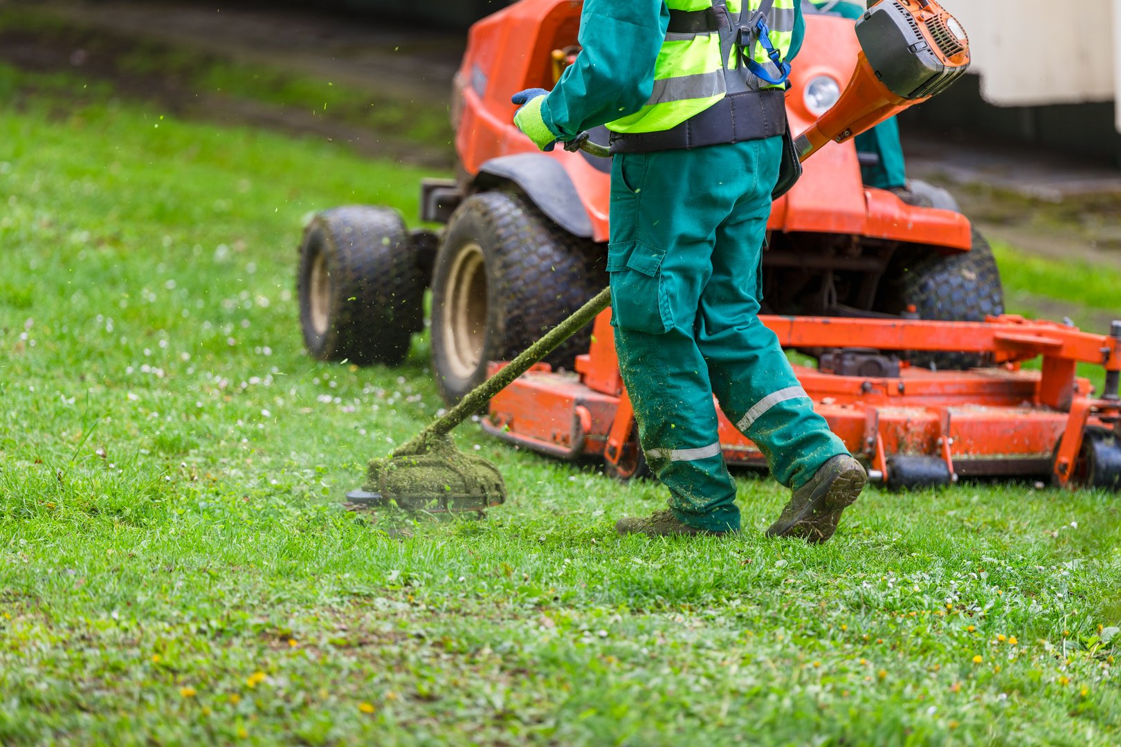 Professional landscaper mowing lawn with a mower and trimming edges with a grass cutter in a park or private property, landscaping maintenance concept