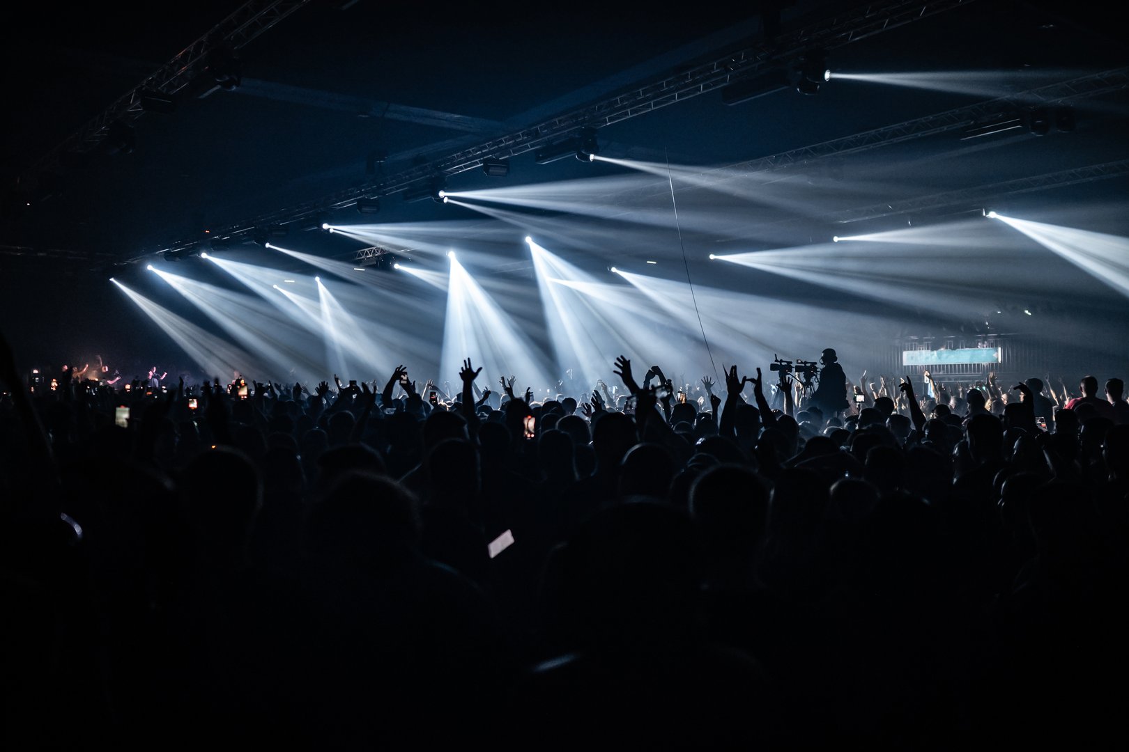 Fans enjoying live music performance, raising hands and cheering under bright stage lights, creating an exciting atmosphere