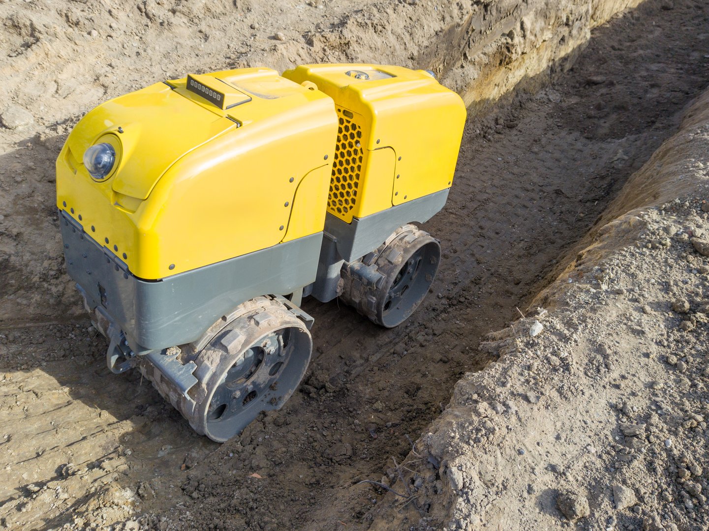 Close up of a yellow remotely controlled trench compactor at a construction site compacting soil