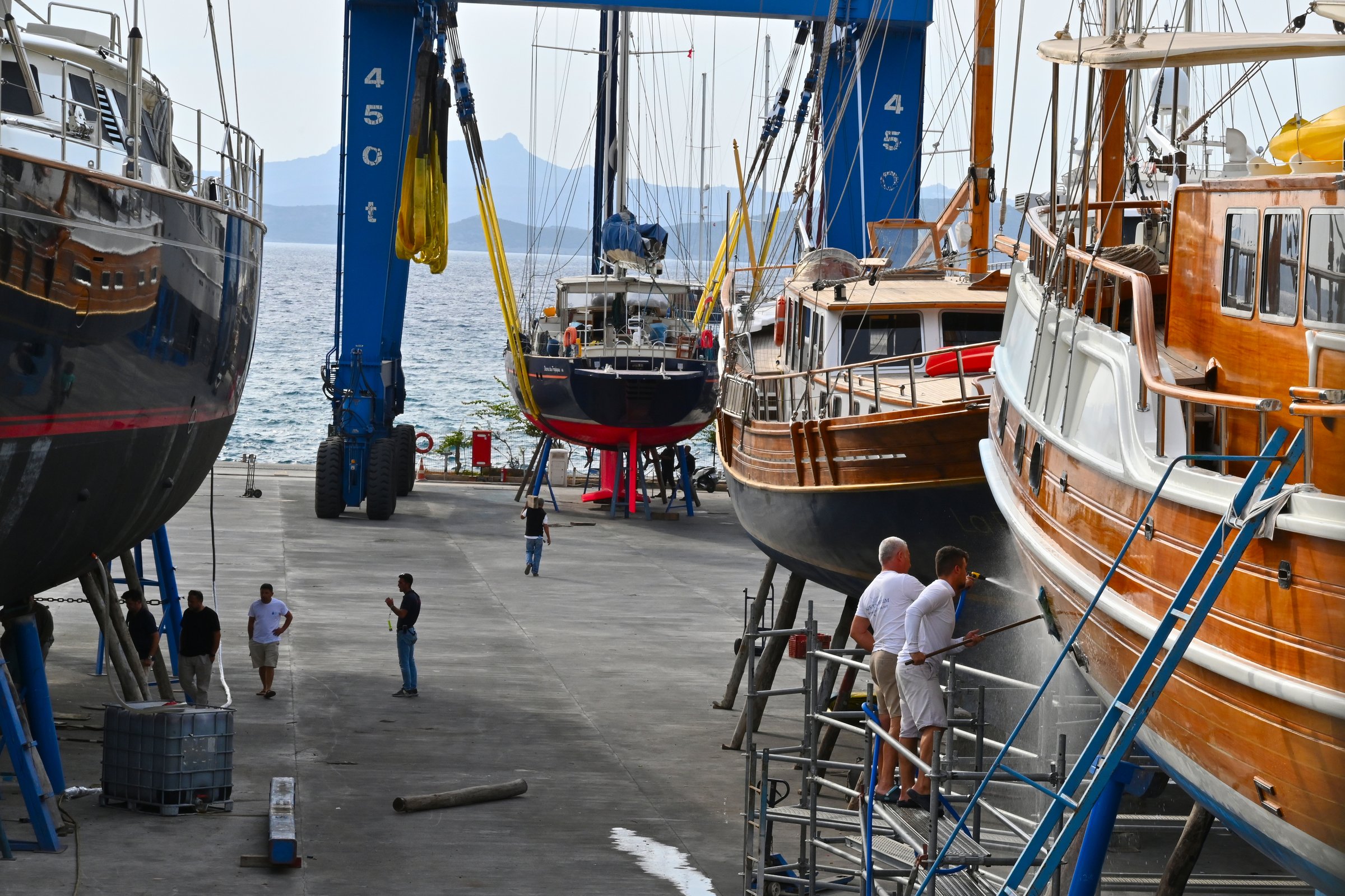 Bodrum, Turkey, 10 14 2024: Two repairman washing hull of wooden sailing boat with masts in Aganlar Marina and shipyard located in Bodrum, the most popular holiday city on the Mediterranean coast.