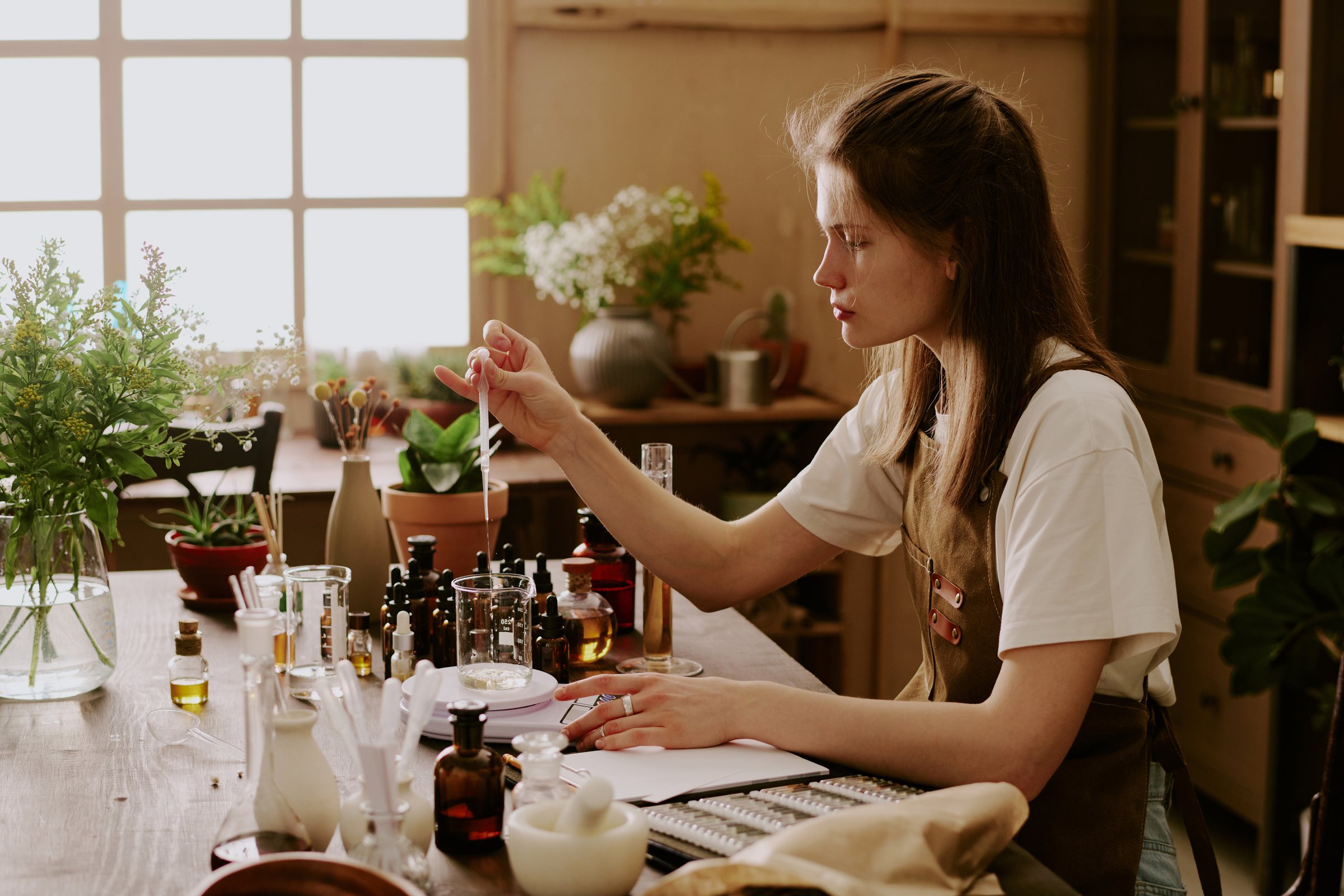 Young perfumer weighing glass flask with organic essence and adding new essential oil