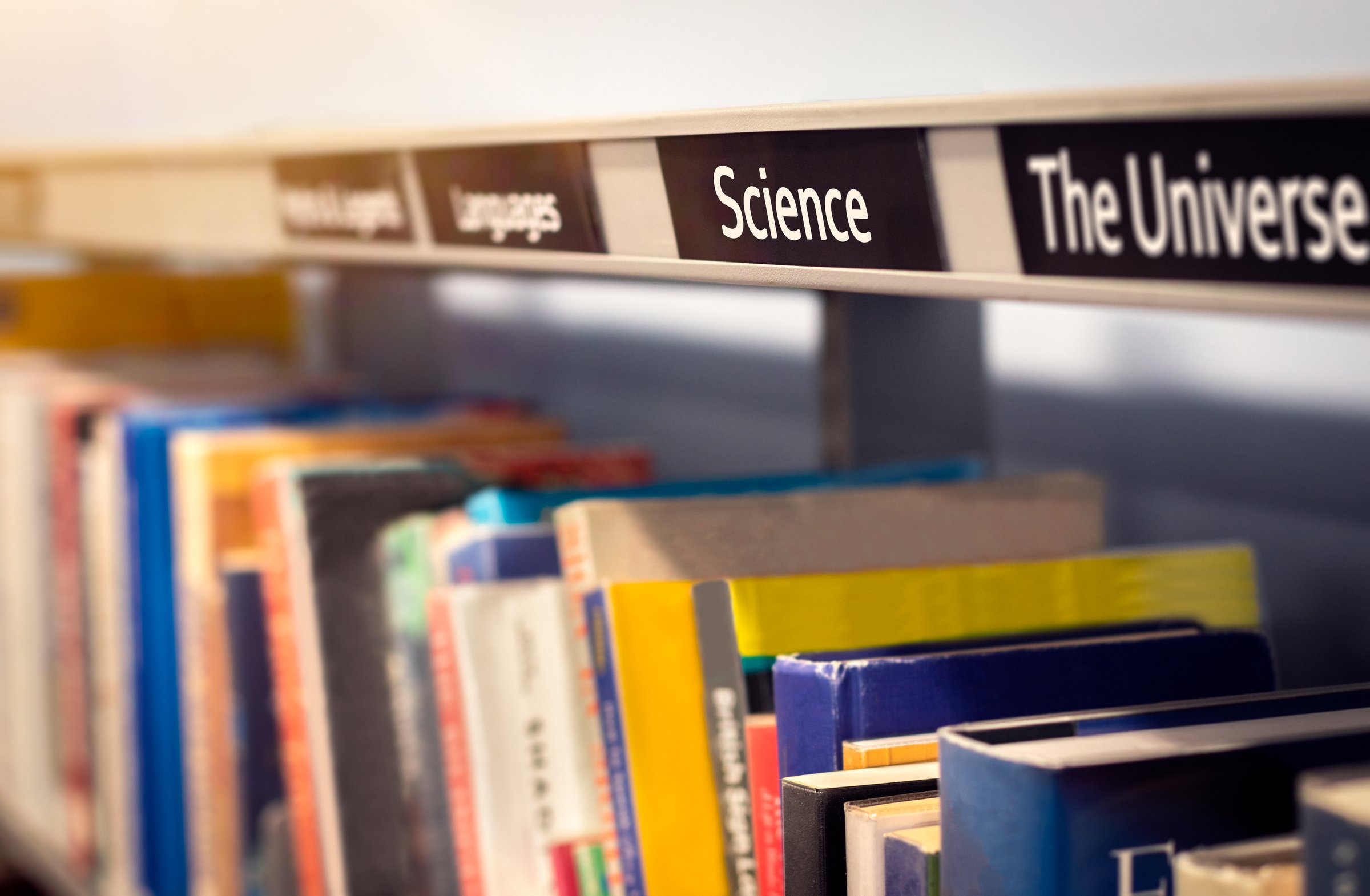Books stacked on shelf under categories of Science and The Universe. Non-fiction library or bookstore scene depicting factual reference books. Concept of knowledge, education and study.