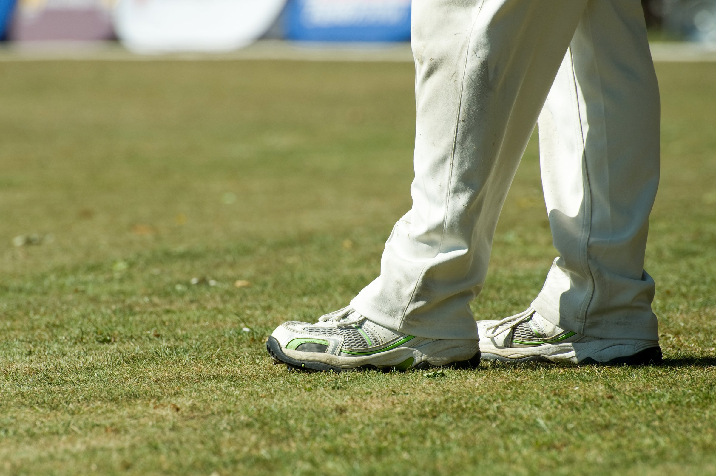 Feet of a cricketer in traditional white trousers.