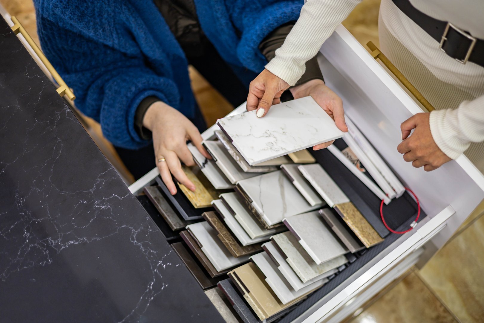 Closeup hands creative female interior designer and customer choosing marble stone color for kitchen or facades. Top view woman client consulting to decorator choice home improvement materials