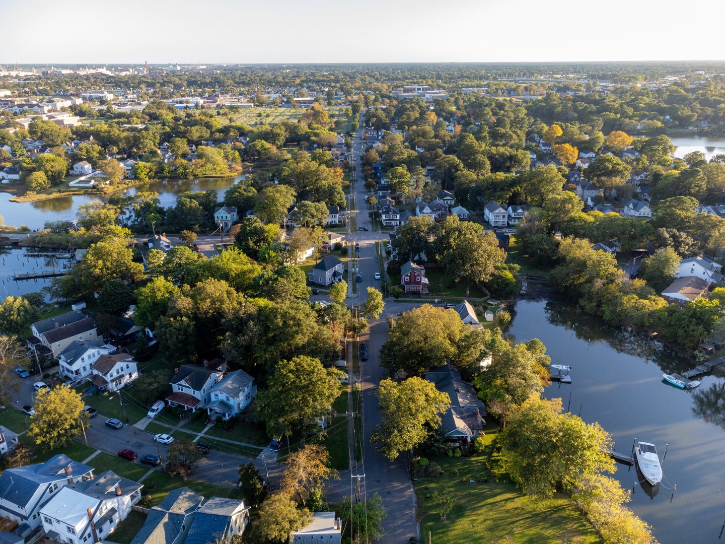 Aerial view of Norfolk, Virginia at sunset showing boats docked along the waterfront and a calm river surrounded by neighborhoods and trees.