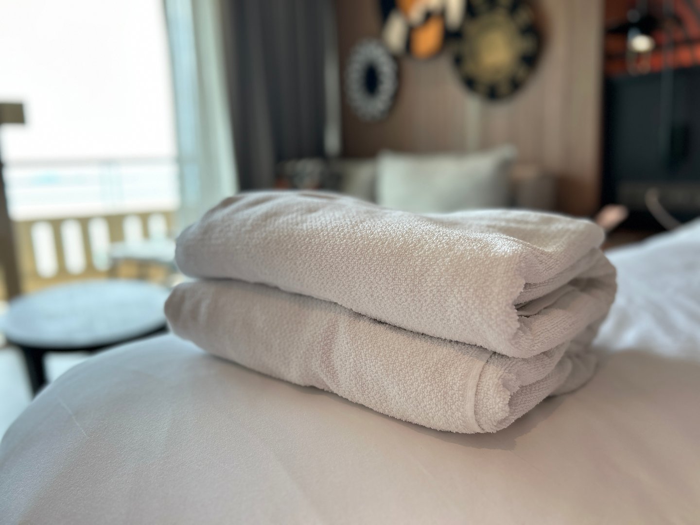 A close up view of two clean white towels folded and stacked on a plush surface likely a bed or pillow in a softly lit hotel room suggesting comfort and hospitality