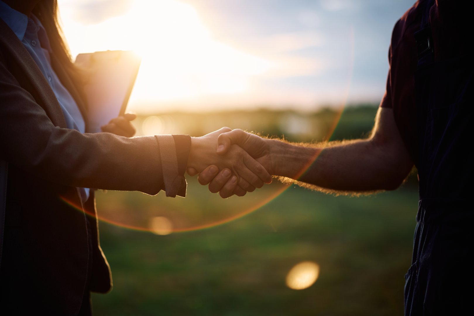 Close up of businesswoman and farm owner shaking hands in the field at sunset.