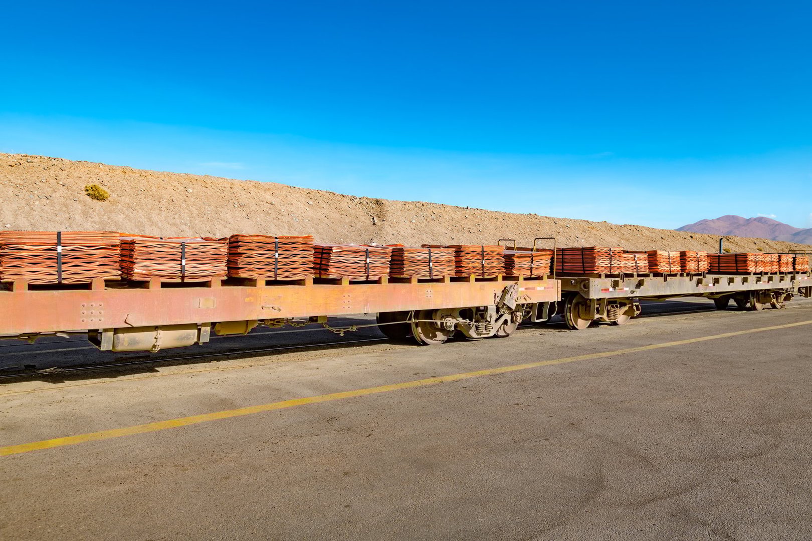 A long train carries stacks of copper cathodes through a vast mining landscape in Chile.