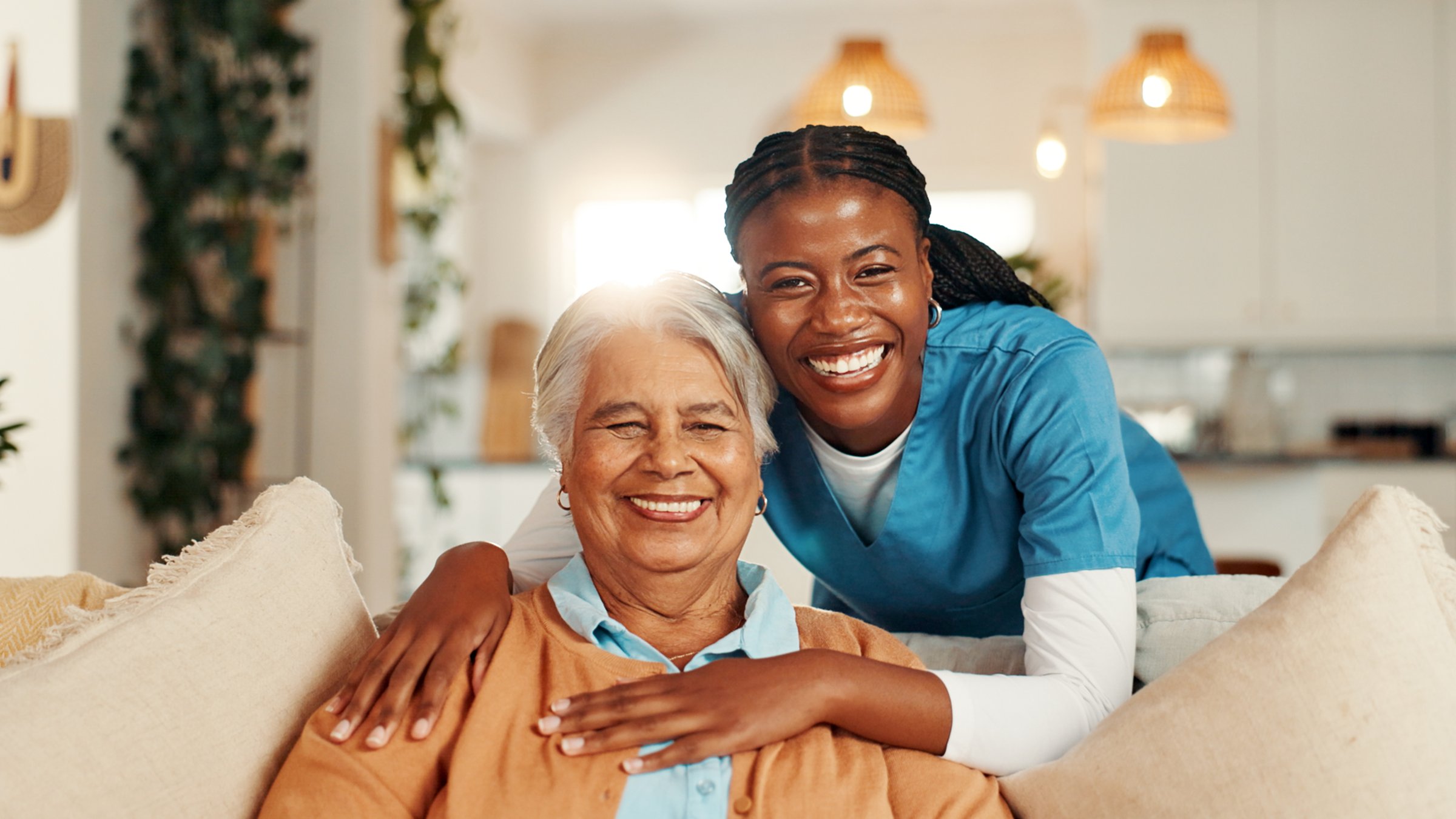 Hugging, portrait and nurse with senior woman for comfort, support or care for good news. Happy, consultation and caregiver embracing elderly female patient on sofa in living room at nursing home.