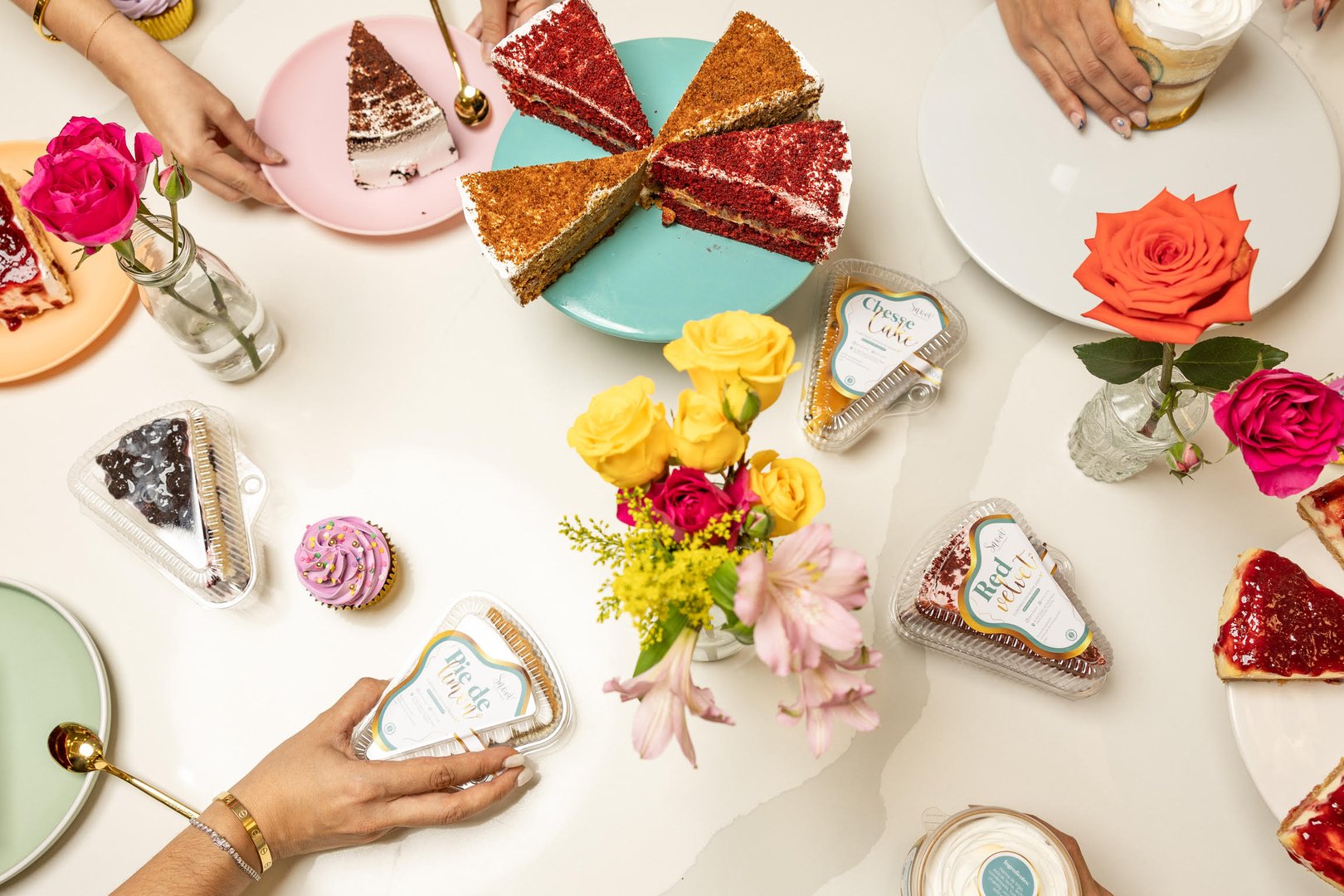 People sharing slices of cake on colorful plates with vibrant flowers on a table.