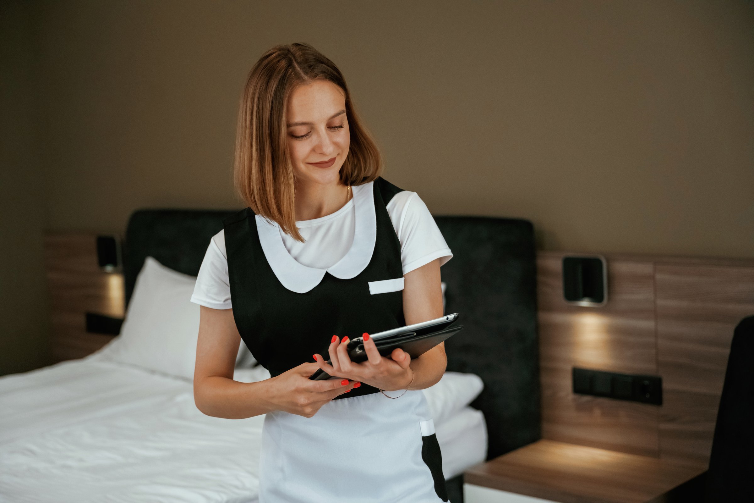 Digital tablet in hands. Young chambermaid is in hotel room.