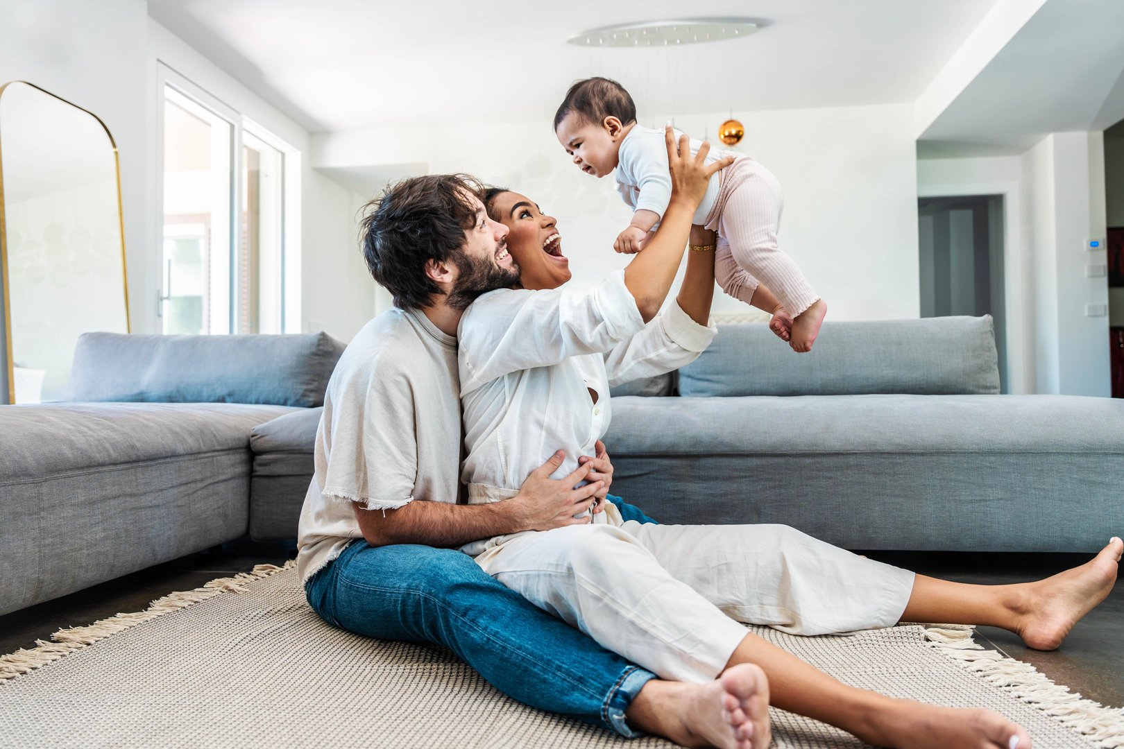 Multiracial husband and wife playing with cute little daughter at home -Cheerful parents embracing beautiful baby children indoors - Family life style concept