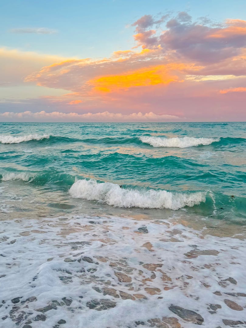 Amazing colorful sky like cotton candy colors.  Clouds and sky meet at horizon. Gentles waves ripple as tide meets the shoreline.  Beautiful natural beauty.