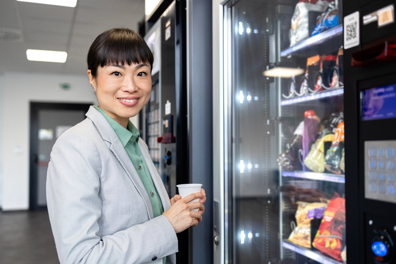 Japanese businesswoman taking a break and buying coffee and snacks on vending machine.