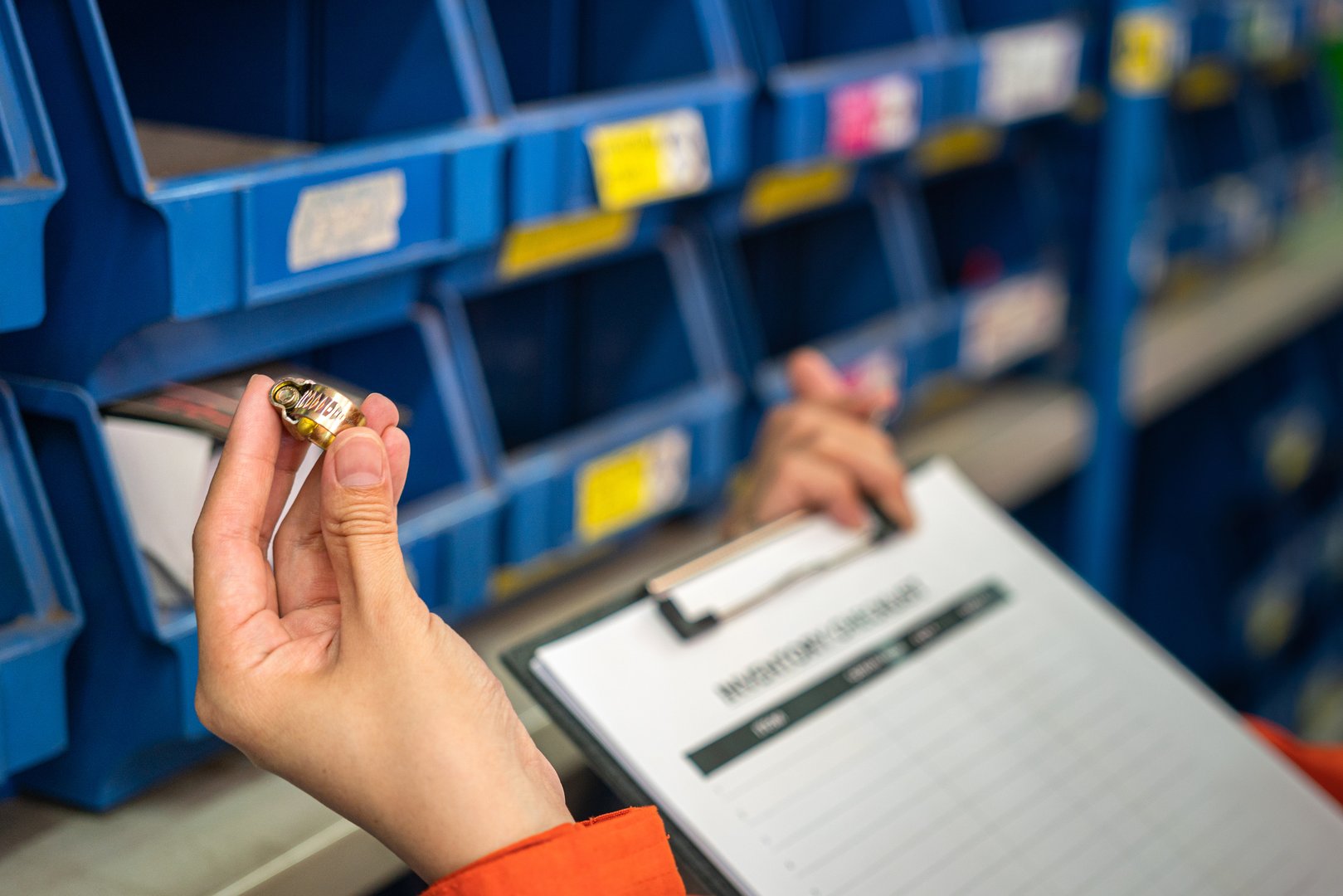 A worker's hand is holding metal ring object, a machinery spare part  with blurred background of storage shelf. Industrial working scene photo, selective focus.