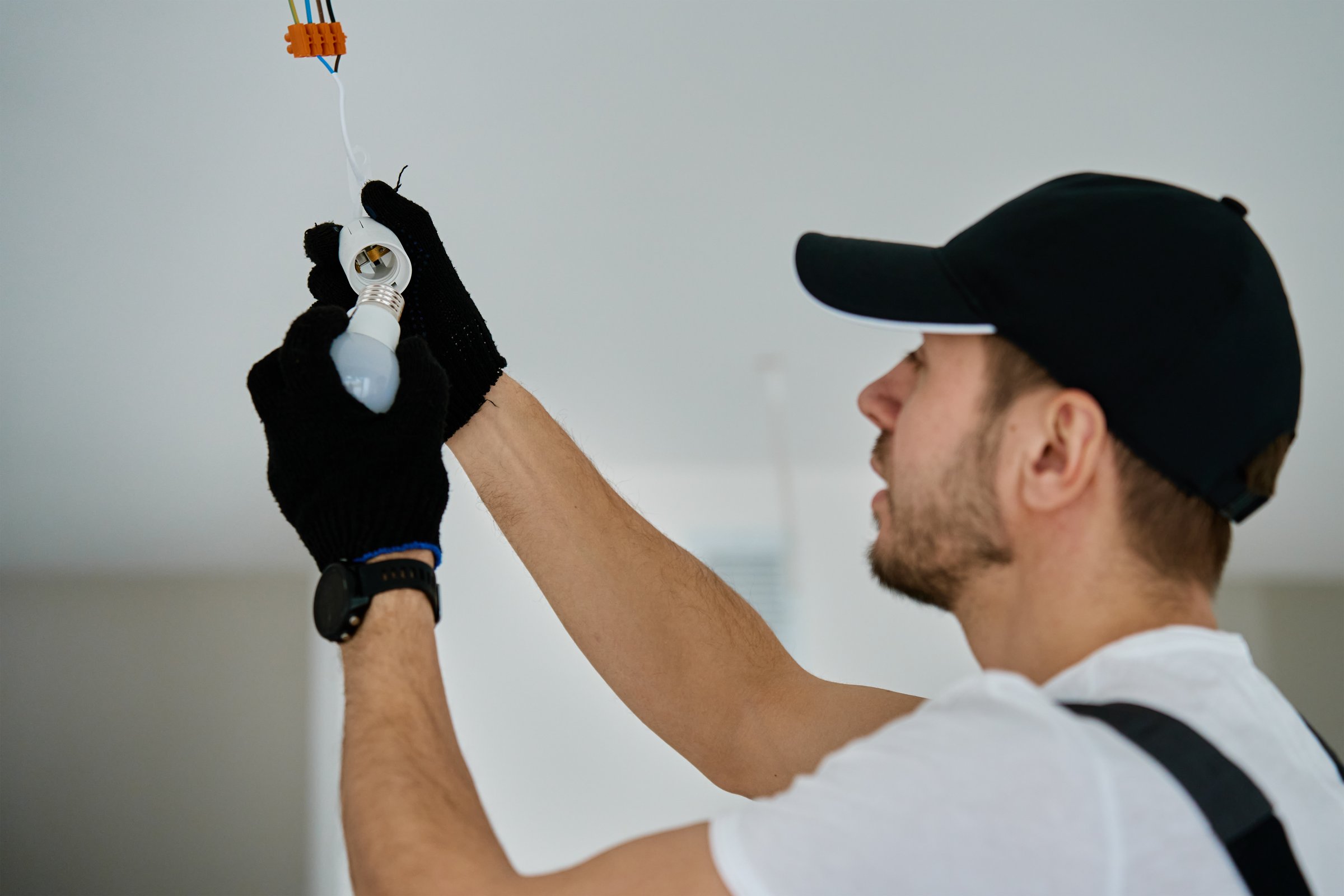 Professional electrician wearing gloves installing light bulb in ceiling socket. Home electrical work during renovation