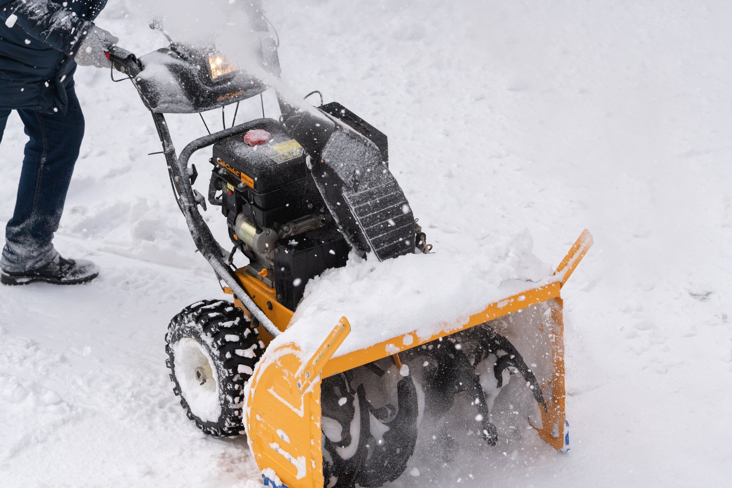 Person using a snowblower to clear snow from a driveway in Anchorage, emphasizing winter maintenance and snow removal services.