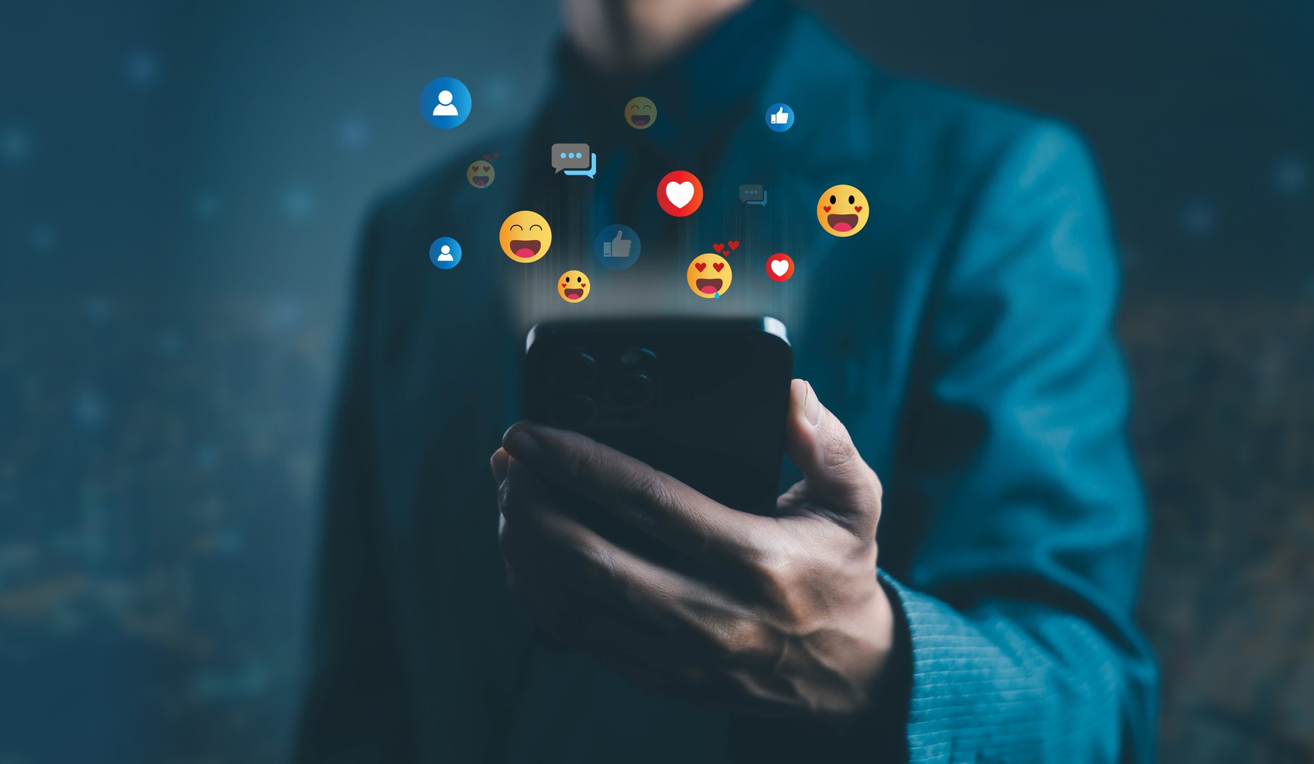 Businessman holding smartphone with floating social media icons such as heart, like, and emoji, symbolizing online communication, digital marketing, and modern social media engagement for business.