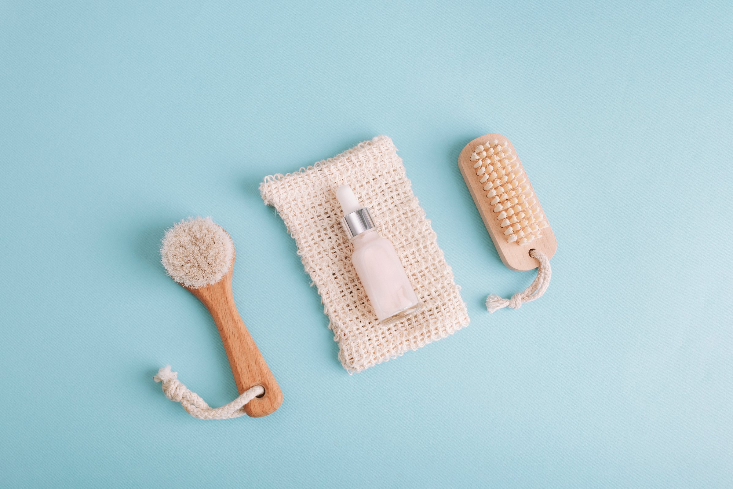 Skincare serum dropper bottle with brushes and sponge on blue background. Flat lay, top view.