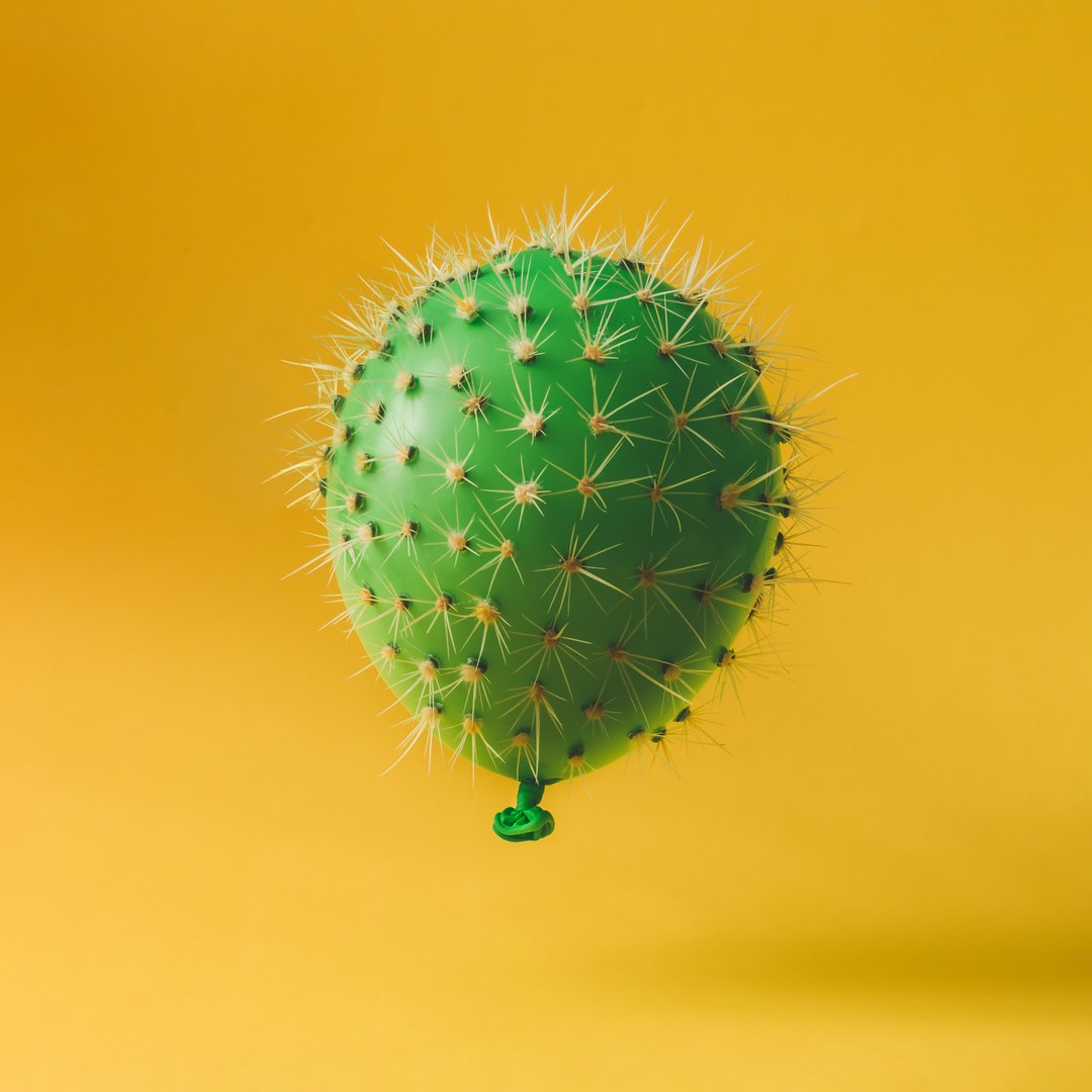 Balloon with cactus needles on bright yellow background. Creative concept.