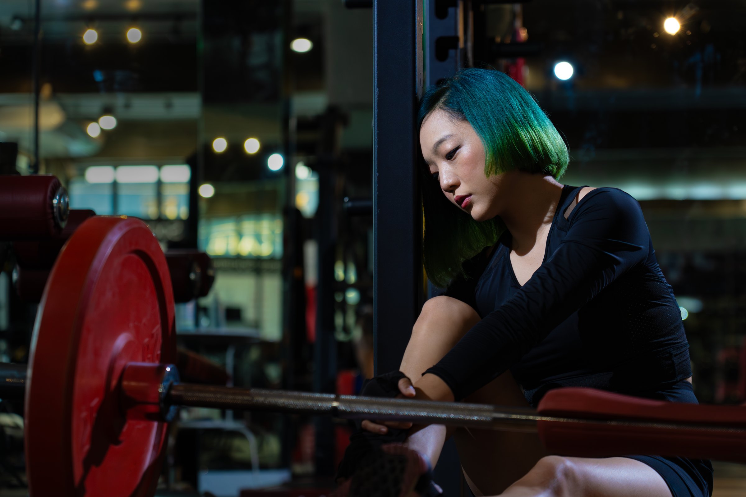 depress athletic asian woman after practicing routine weightlifting and overtraining at modern gym, active fitness people suffer pain injury accident from workout weight training in dark sport club