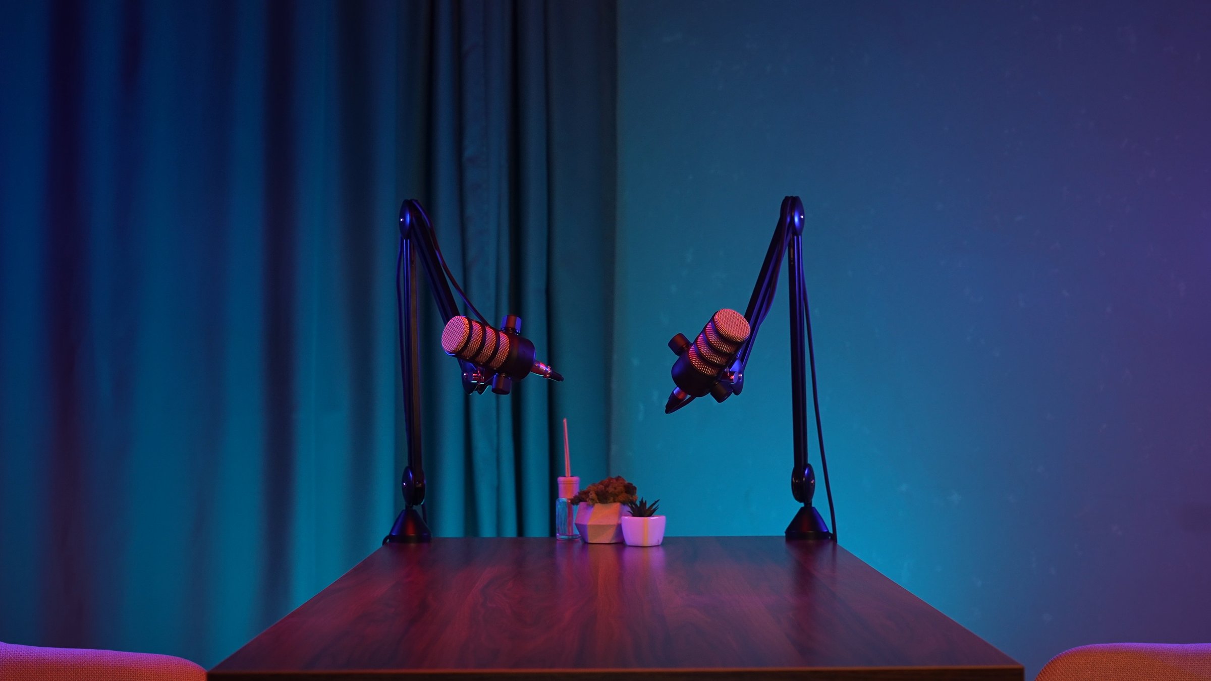 Inside a stylish podcast studio, two microphones stand poised over a wooden table.