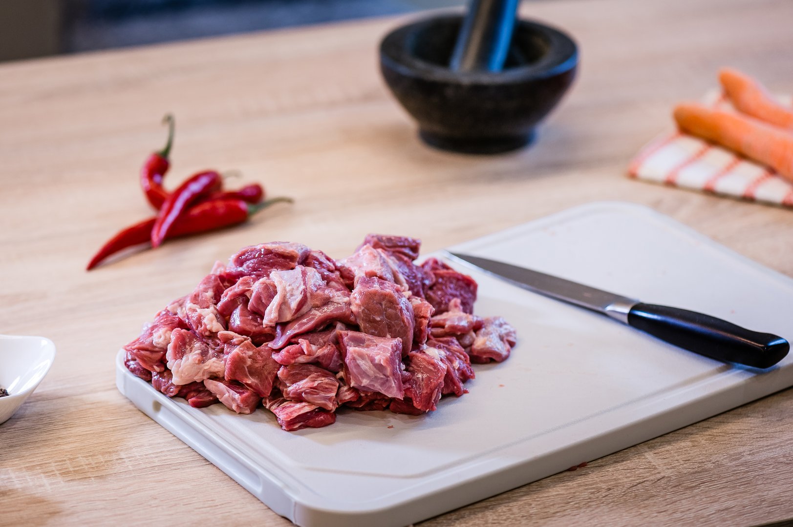 Raw beef meat chopped in cubes with knife, carrots, chili pepper and spices on cutting board. Cook recipe step-by-step. Pilaf recipe in pictures.