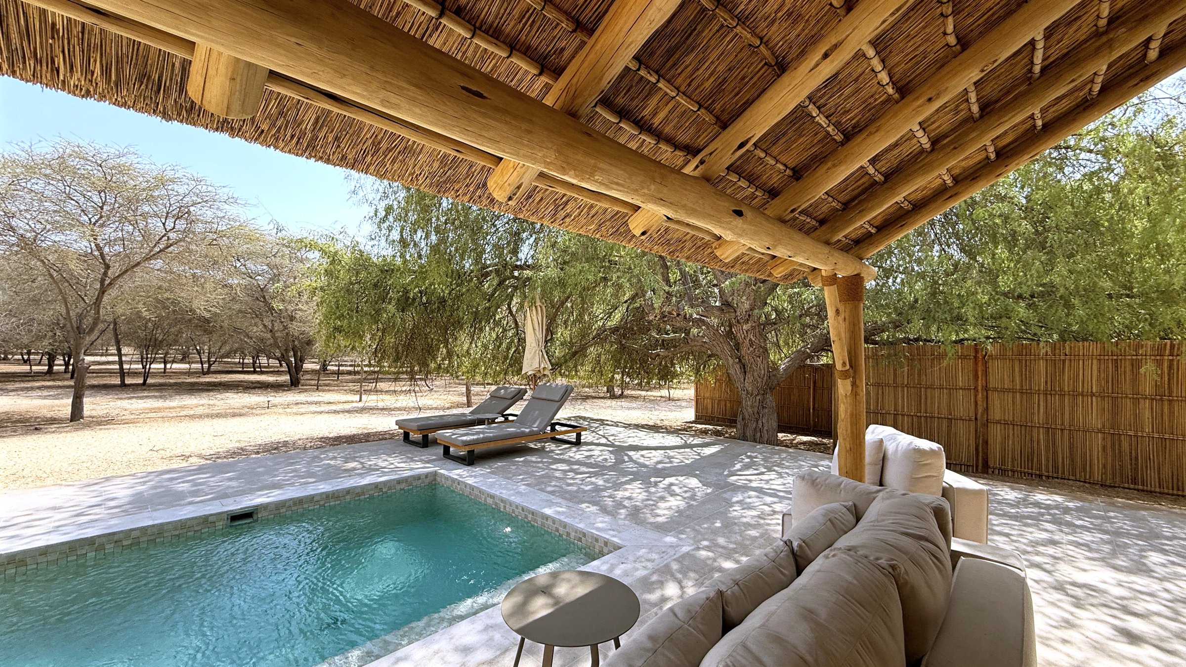 Tranquil desert oasis retreat featuring private pool, comfortable lounge area under thatched roof, and serene landscape, creating an idyllic vacation setting