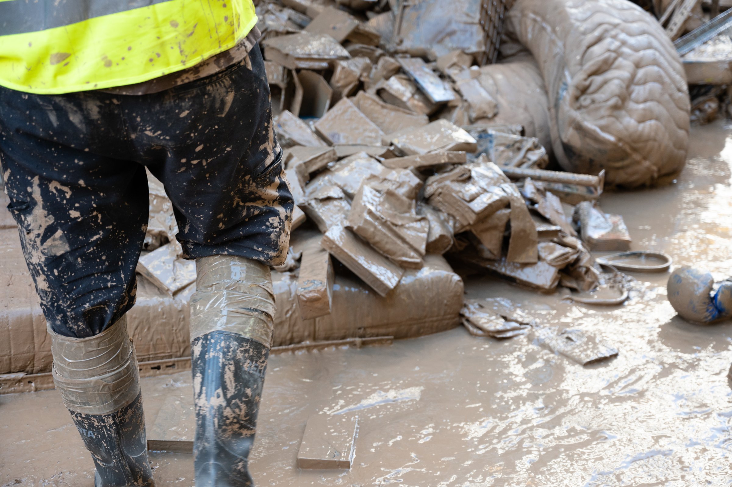 Person in boots standing on a muddy site with debris after a flood in Valencia, Spain