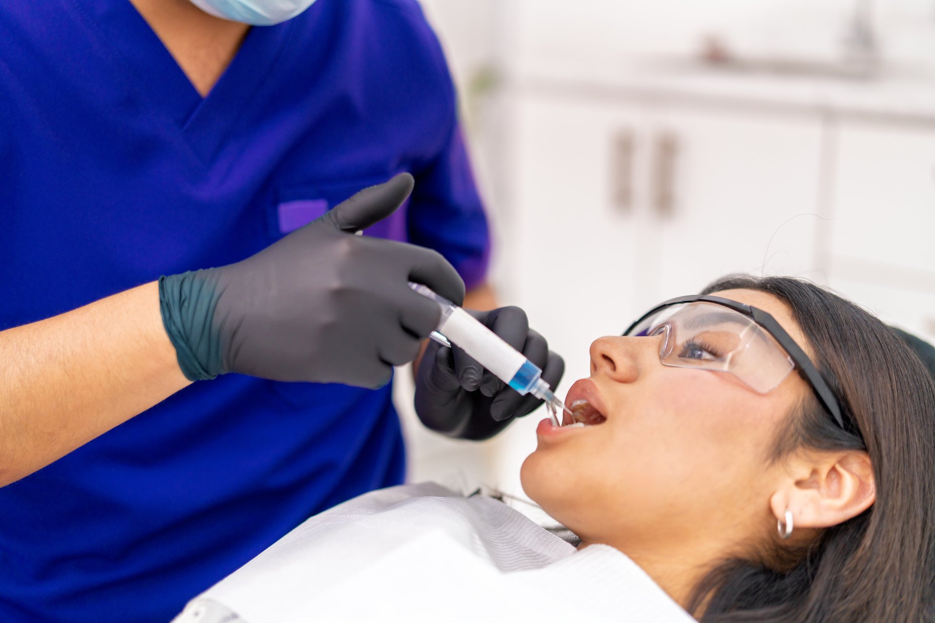 Dentist performing a professional dental procedure, applying bright blue gel onto a young adult patient's teeth in a clinic