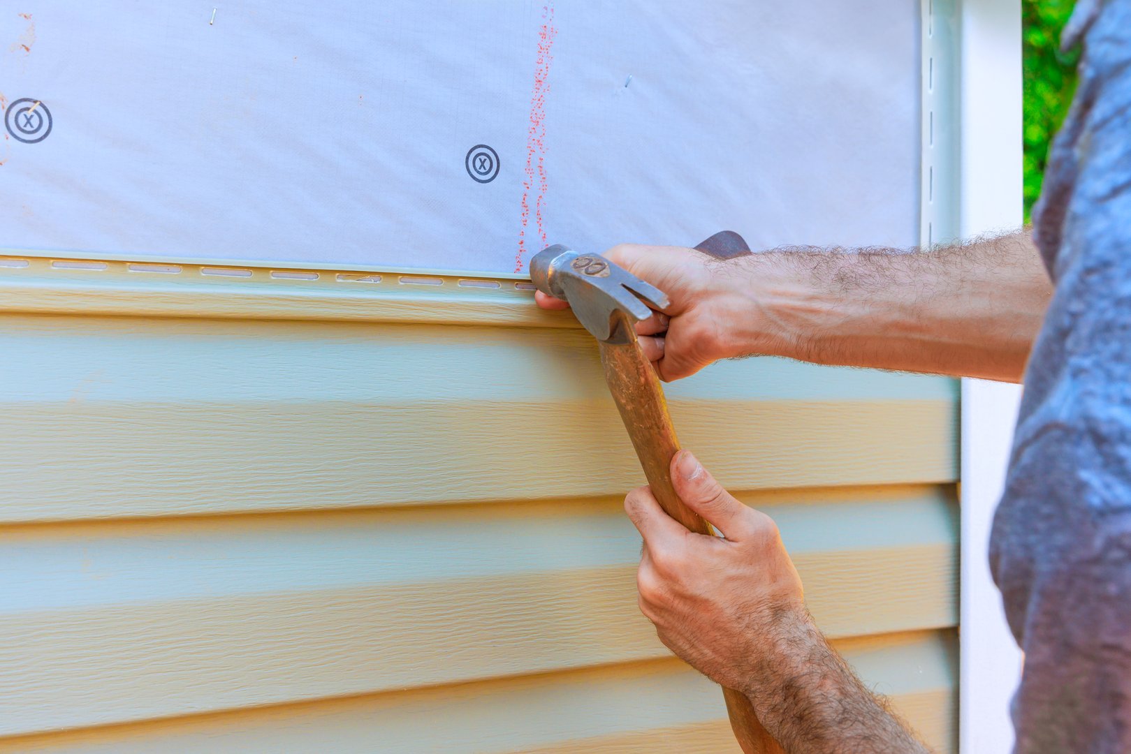 Worker is using hammer to secure new PVC vinyl siding while working on home renovation project outside.