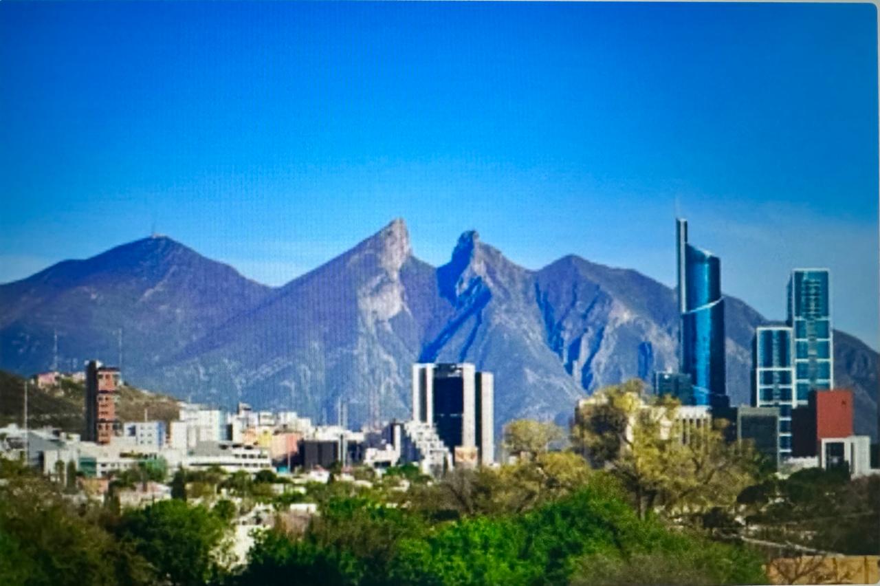 City skyline with modern buildings in front of a mountain range under a clear blue sky.