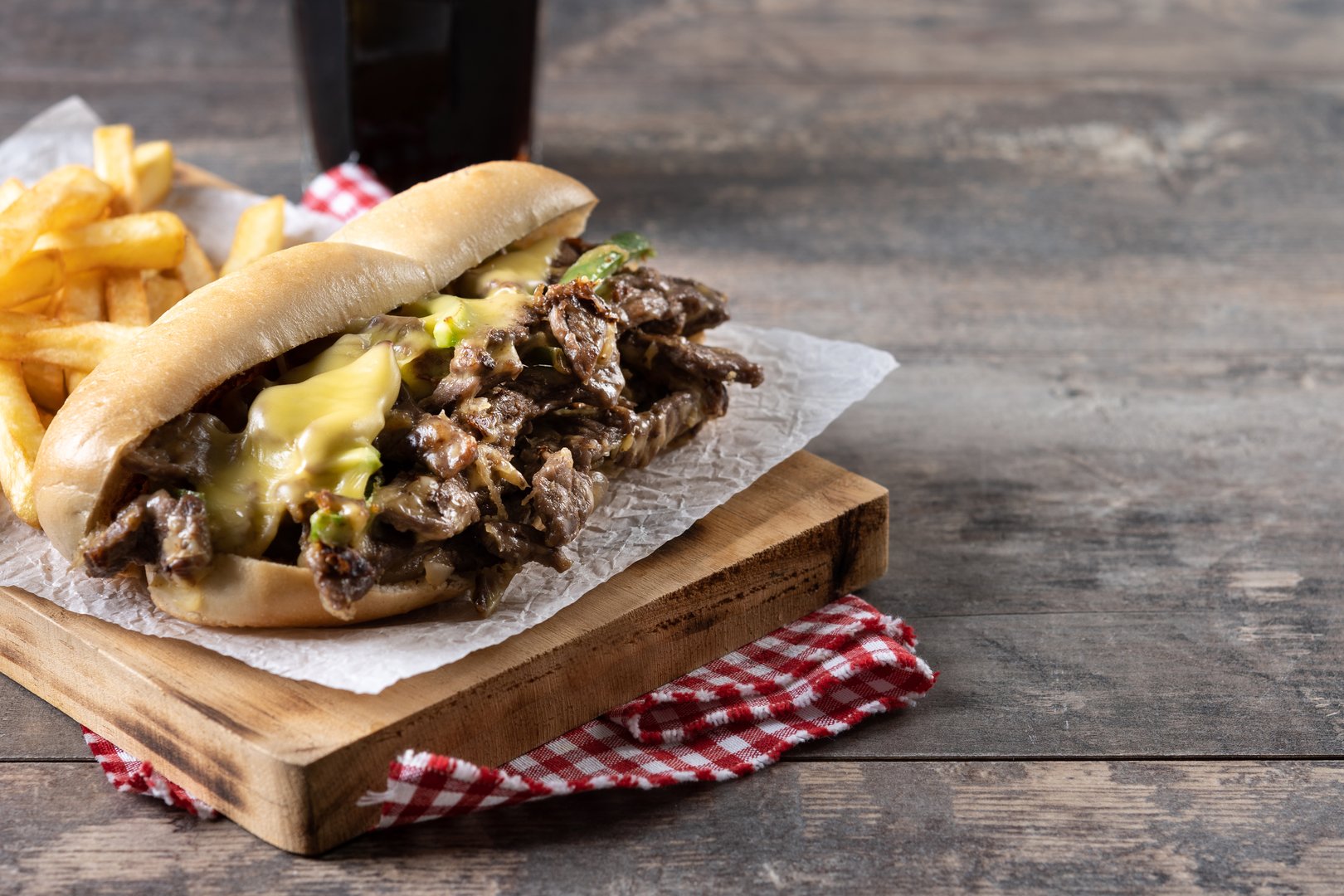 Philly cheesesteak sandwich with beef, cheese,green pepers and caramelized onion on wooden table