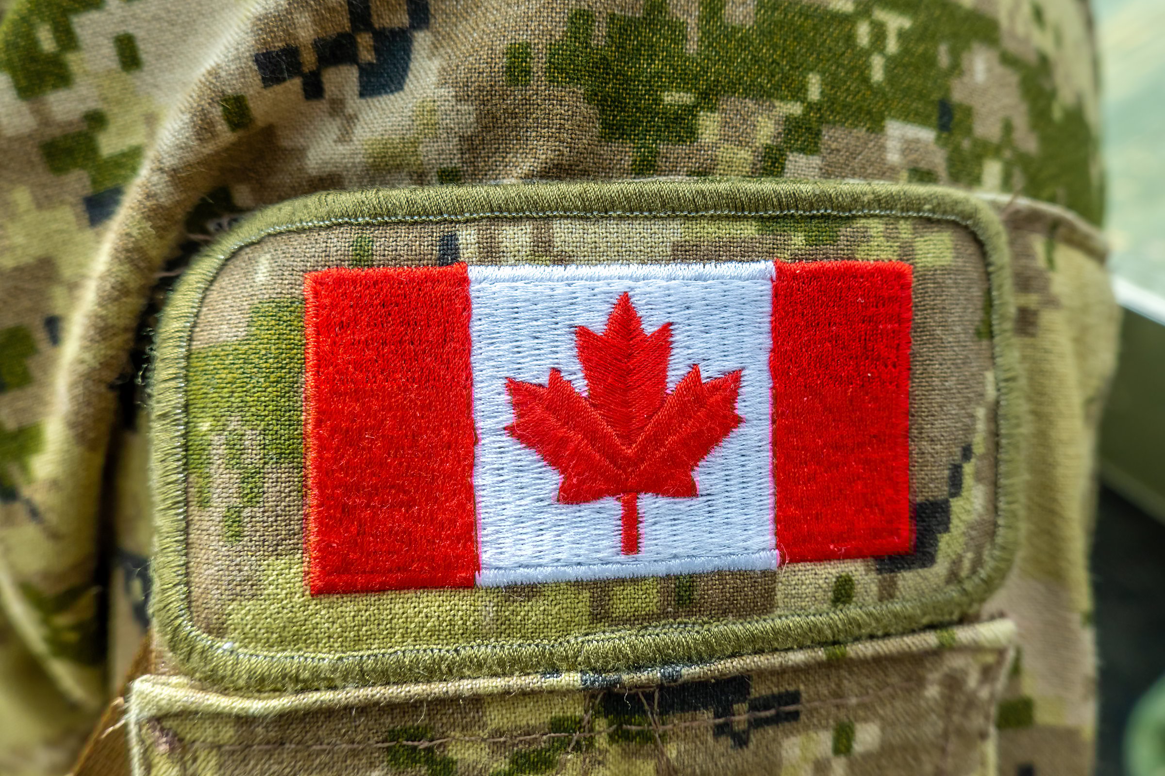 A close-up of a Canadian flag patch on a military camouflage uniform, symbolizing national service, identity, and pride.