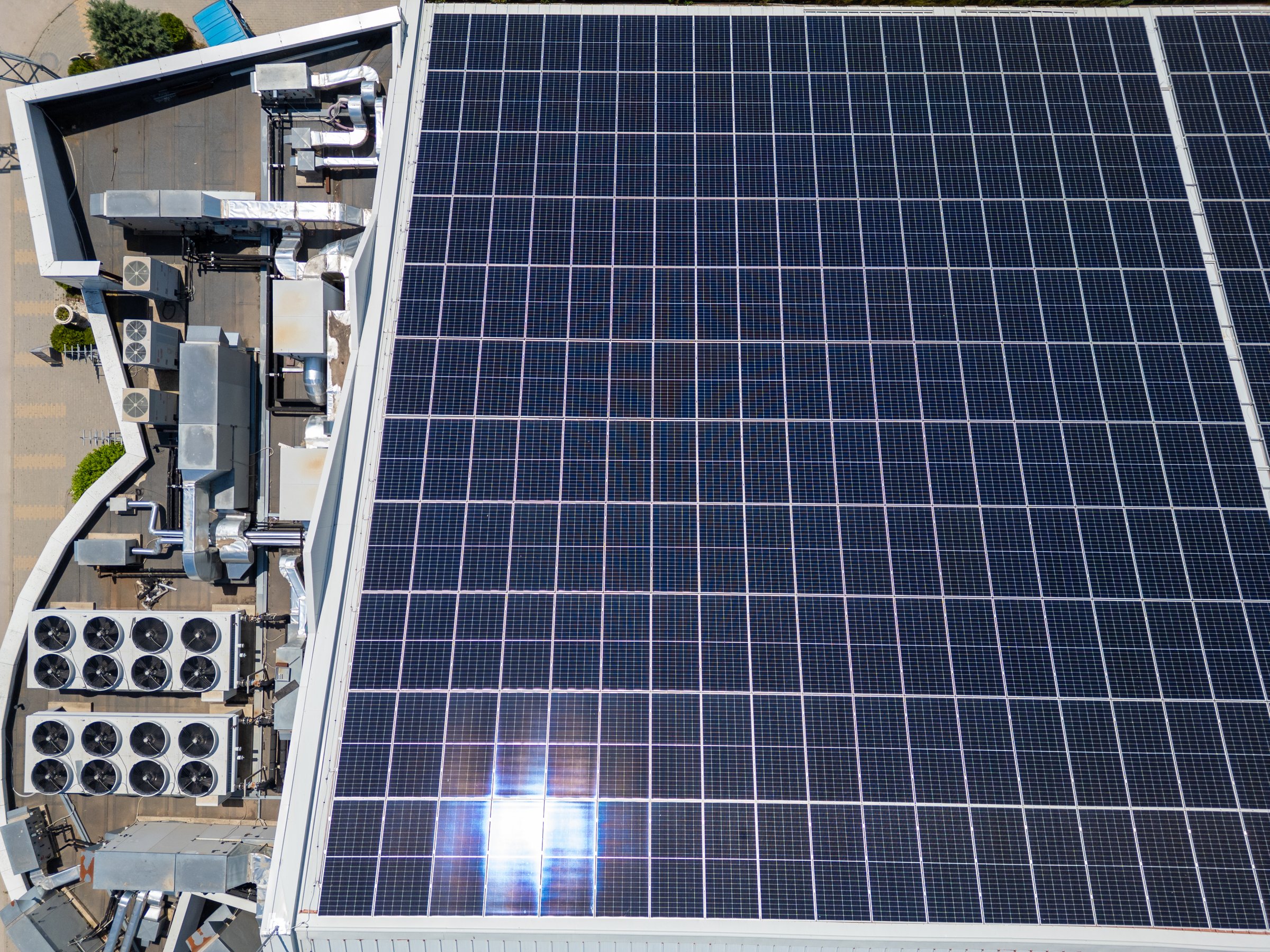 Aerial top-down view of industrial rooftop with solar panels and HVAC systems. Renewable energy and modern ventilation technology for sustainable building infrastructure.