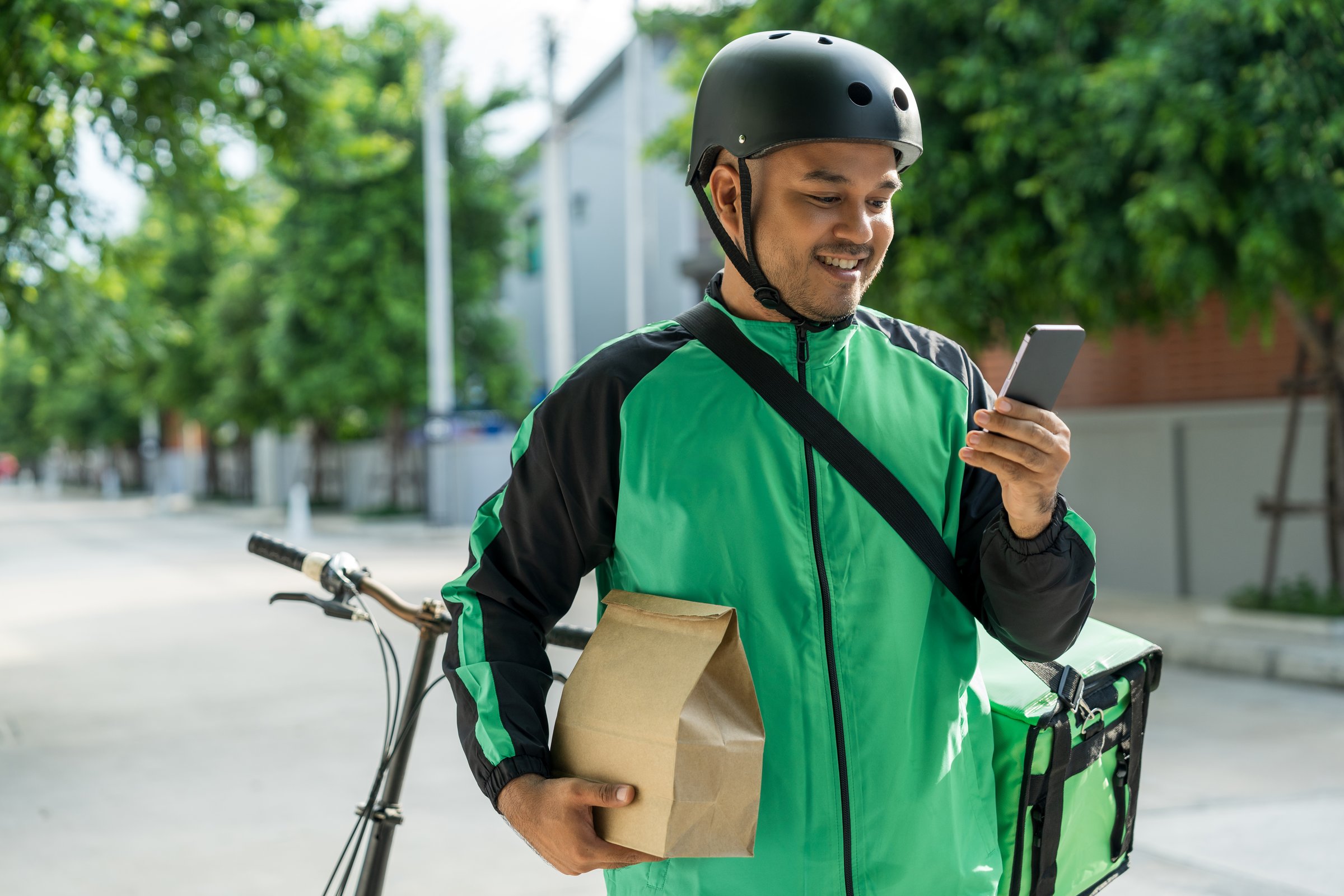 Portrait Rider food delivery man wearing green uniform and helmet cycling a bicycle the food service to customer. Happy delivery man with green backpack shipping of goods to customers.